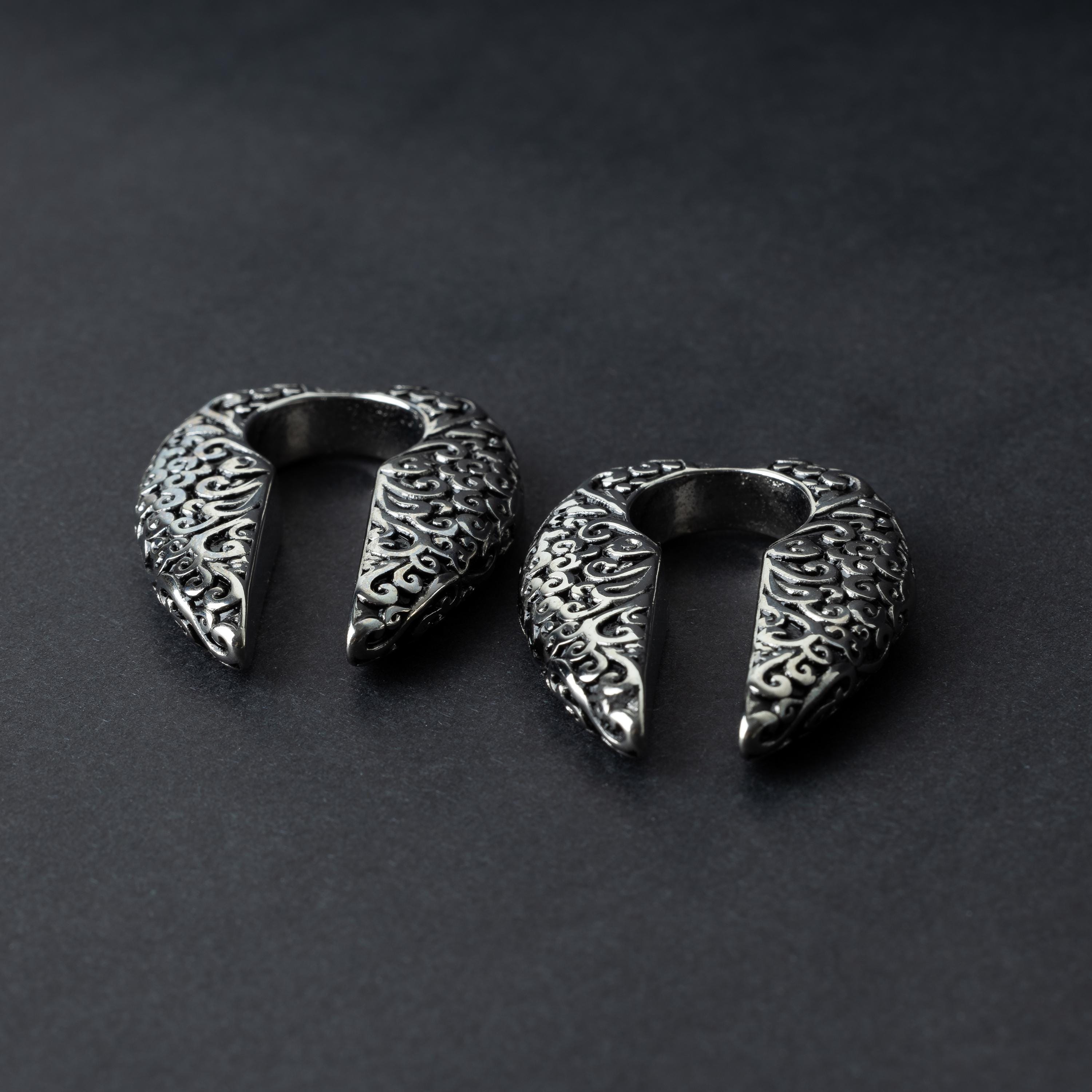 A pair of split ear weights in polished silver with detailed filigree patterns, displayed on a dark background.