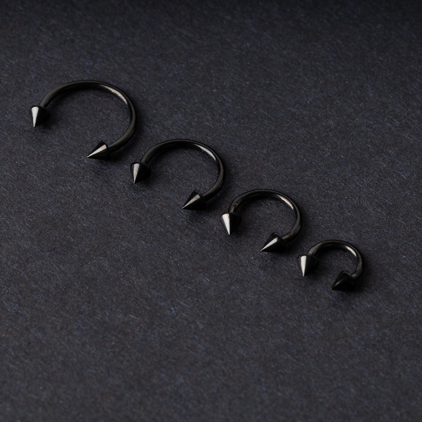 Four G23 titanium black horseshoe rings with spiked ends in varying sizes, displayed on a dark background showcasing their polished finish.