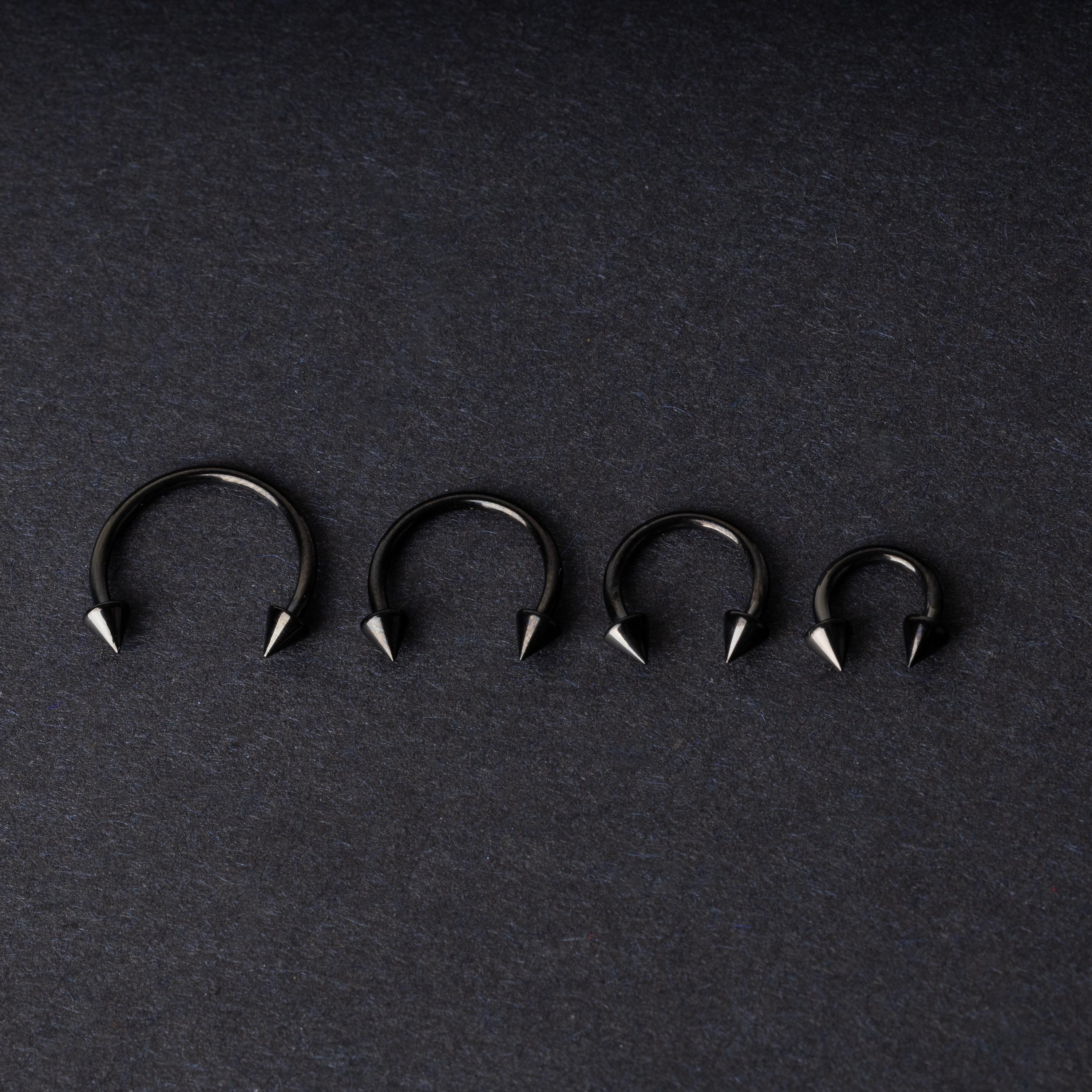 Four G23 titanium black horseshoe rings with spiked ends in varying sizes, displayed on a dark background showcasing their polished finish.