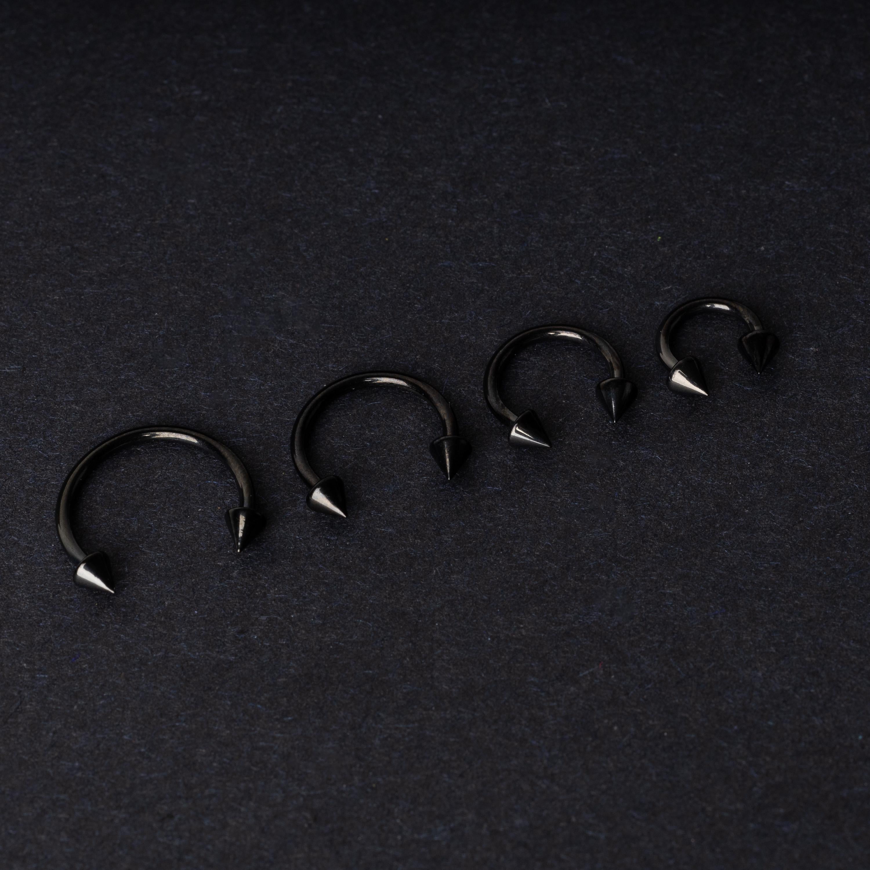 Four G23 titanium black horseshoe rings with spiked ends in varying sizes, displayed on a dark background showcasing their polished finish.