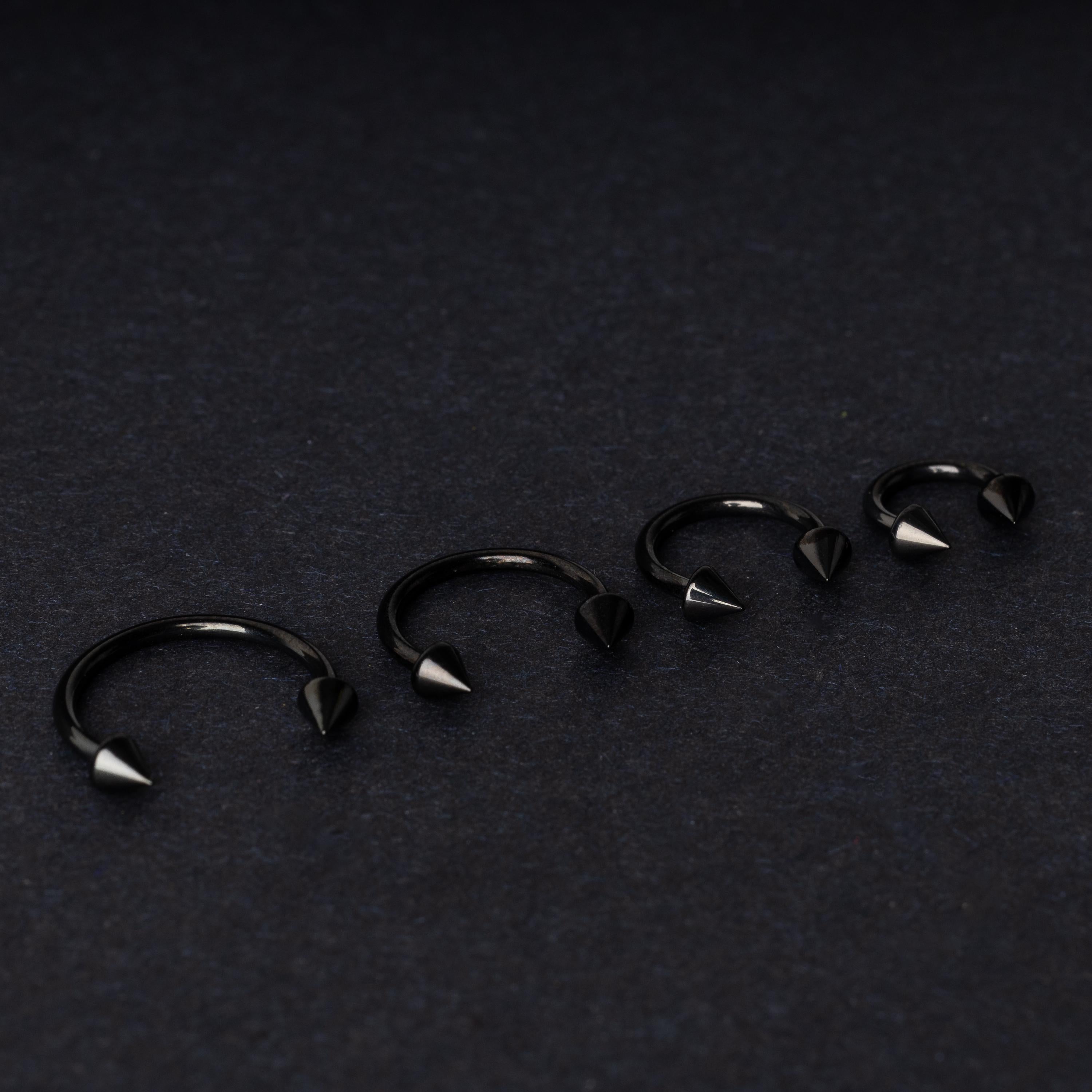 Four G23 titanium black horseshoe rings with spiked ends in varying sizes, displayed on a dark background showcasing their polished finish.