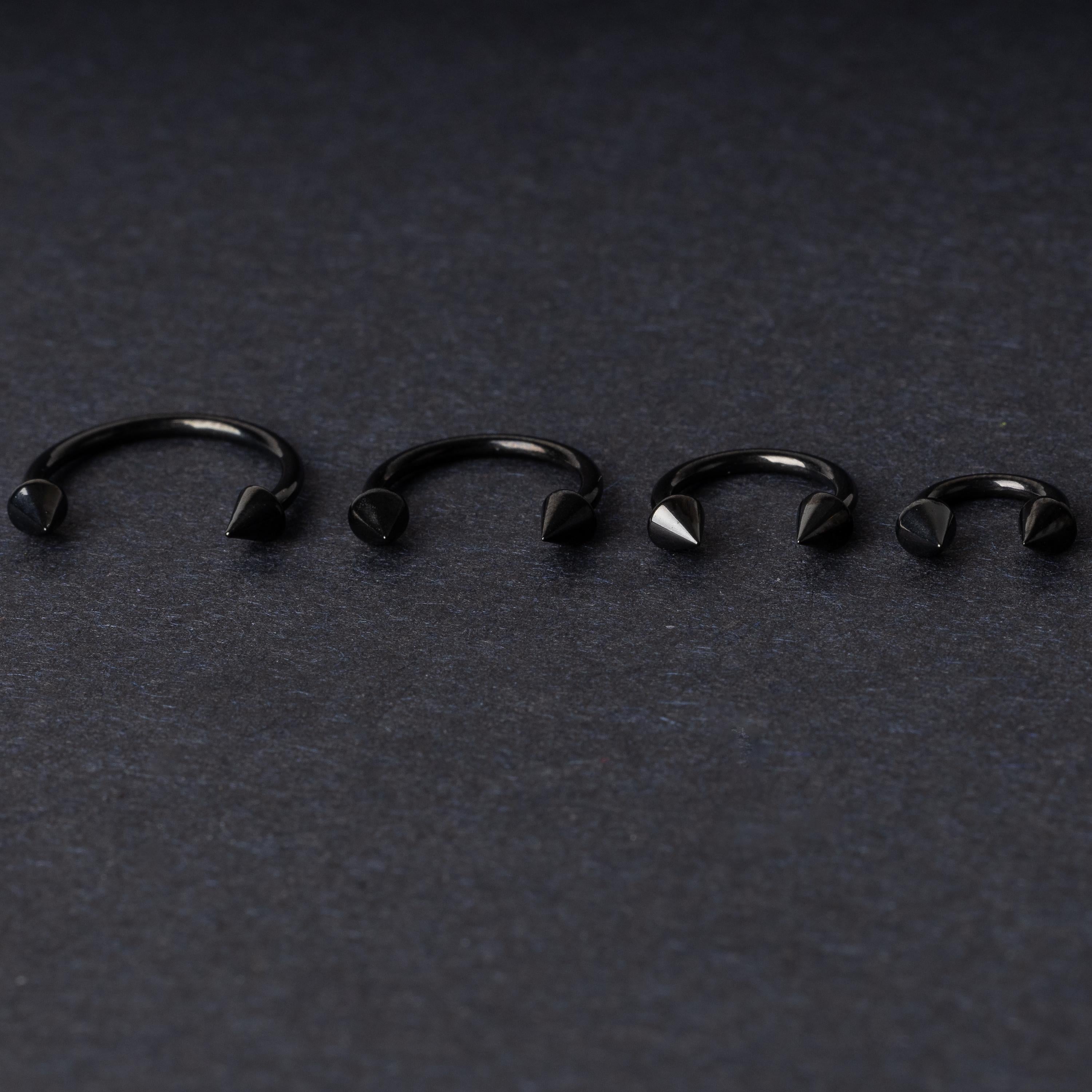 Four G23 titanium black horseshoe rings with spiked ends in varying sizes, displayed on a dark background showcasing their polished finish.