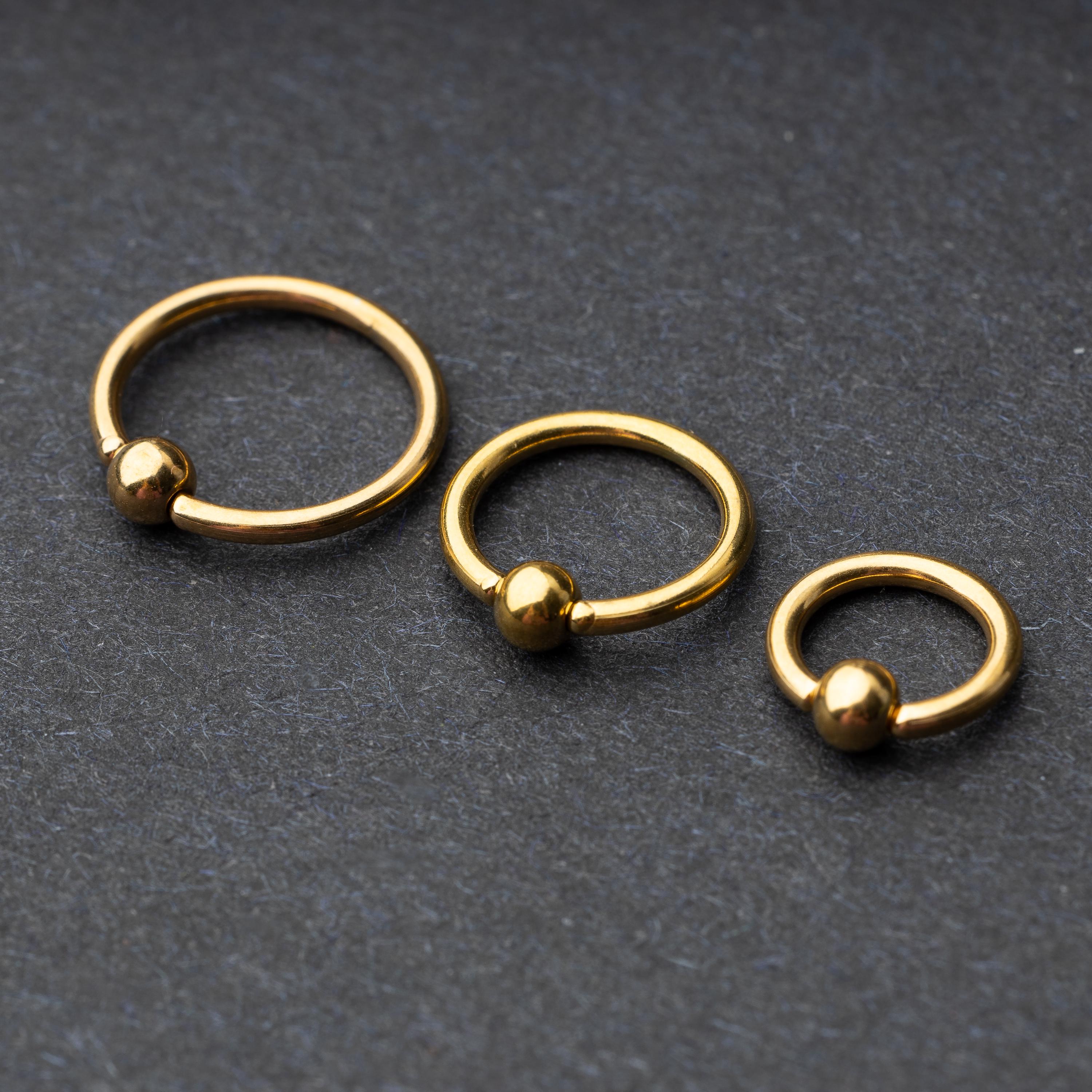 Three gold-tone stainless steel captive bead rings of varying sizes displayed on a dark background.