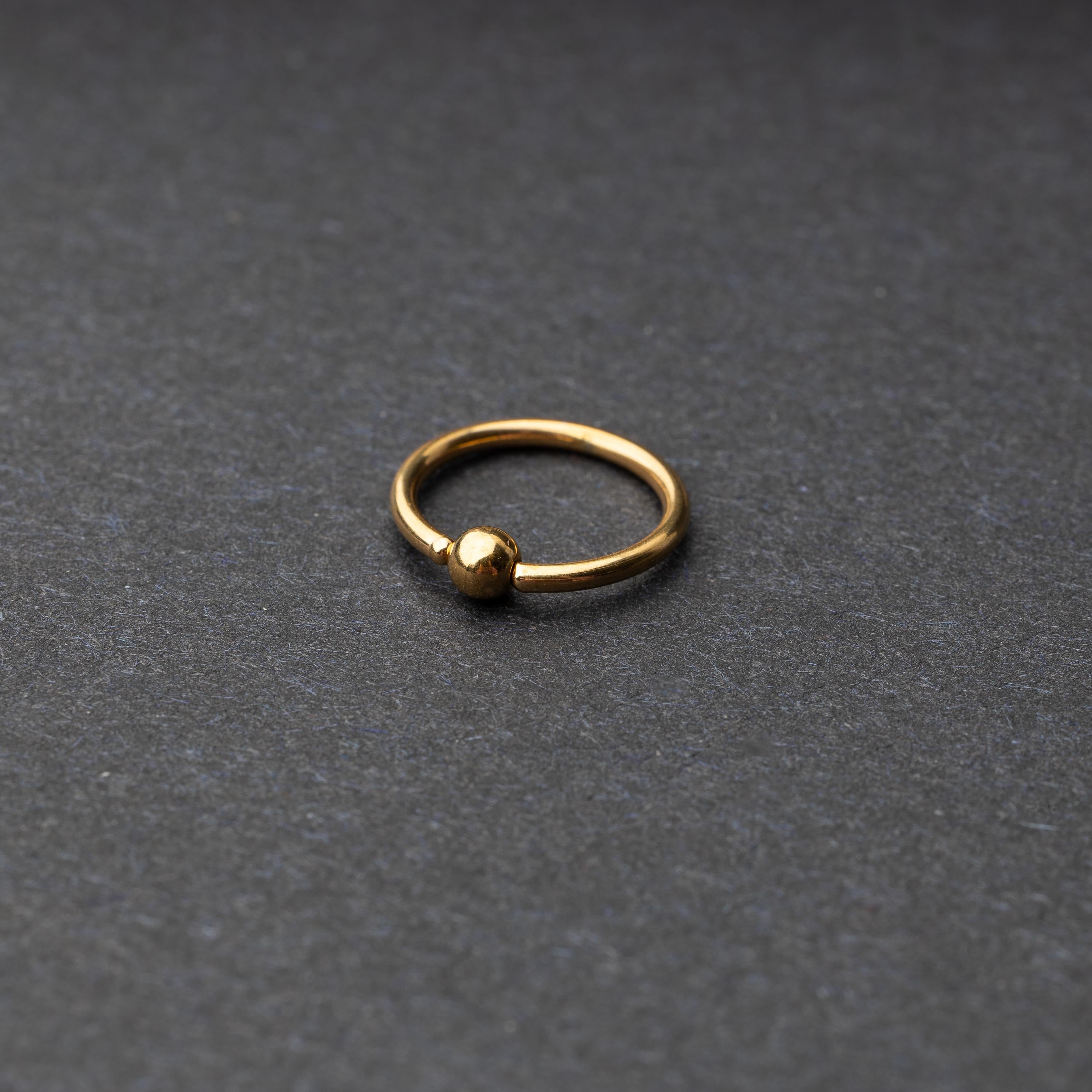 A gold-tone stainless steel captive bead rings displayed on a dark background.