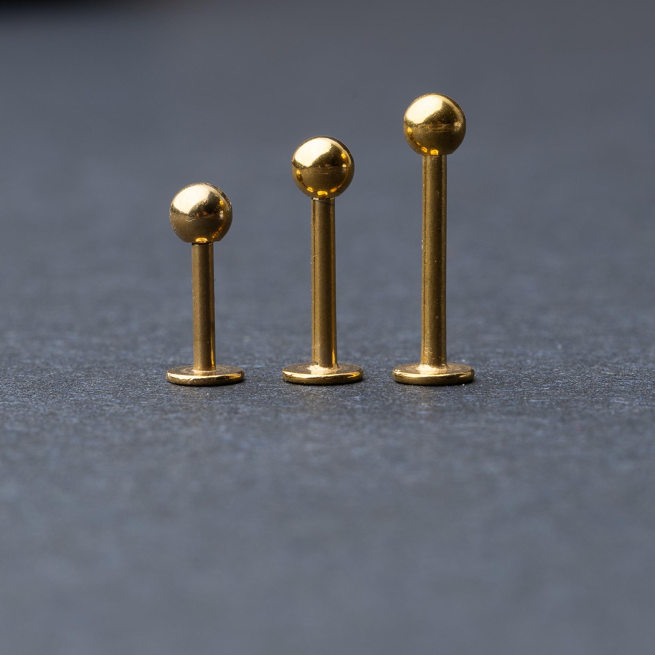 Gold labret studs with ball ends in three different lengths, displayed on a dark background.