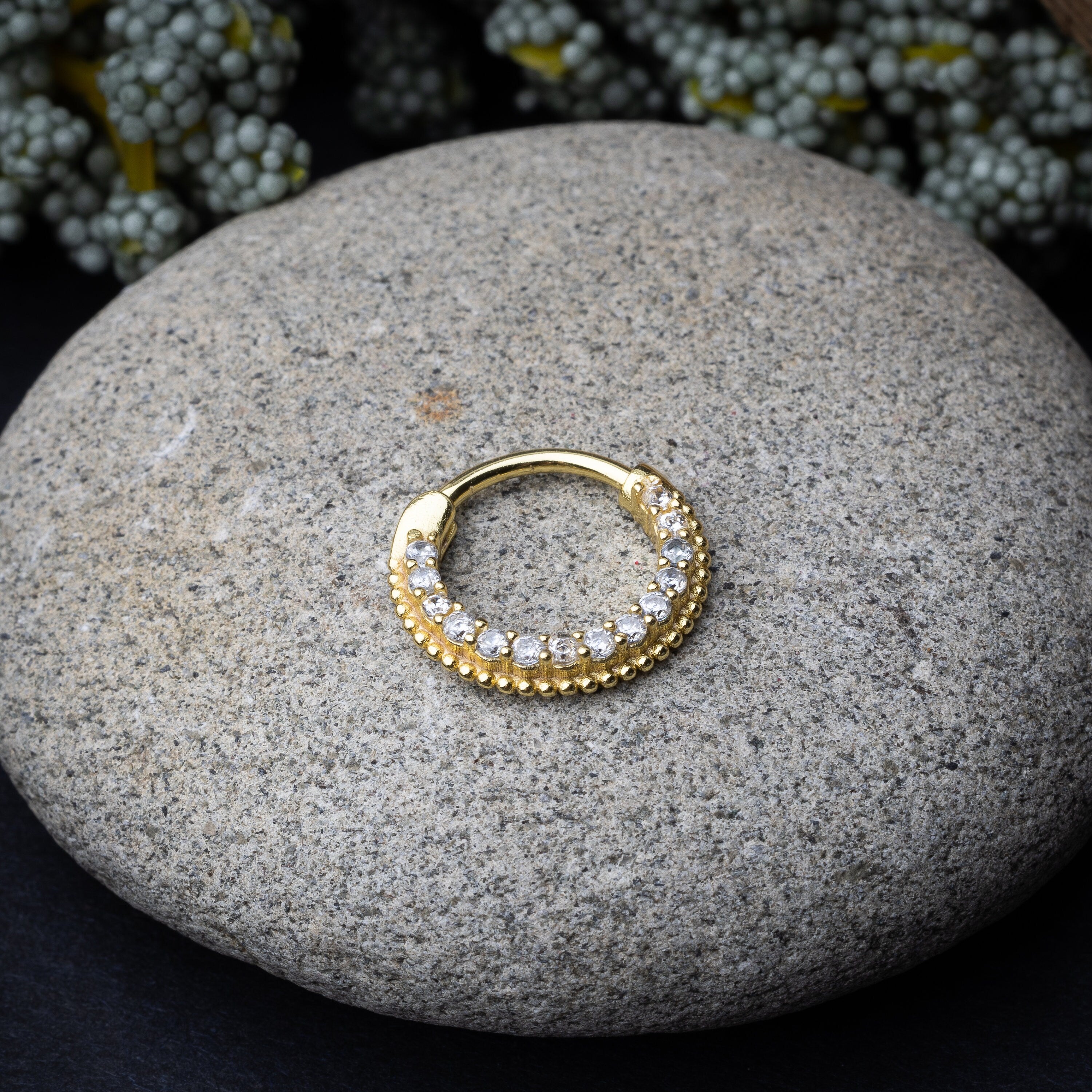 Stainless steel clicker with double rows of clear gemstones in gold displayed on a stone background