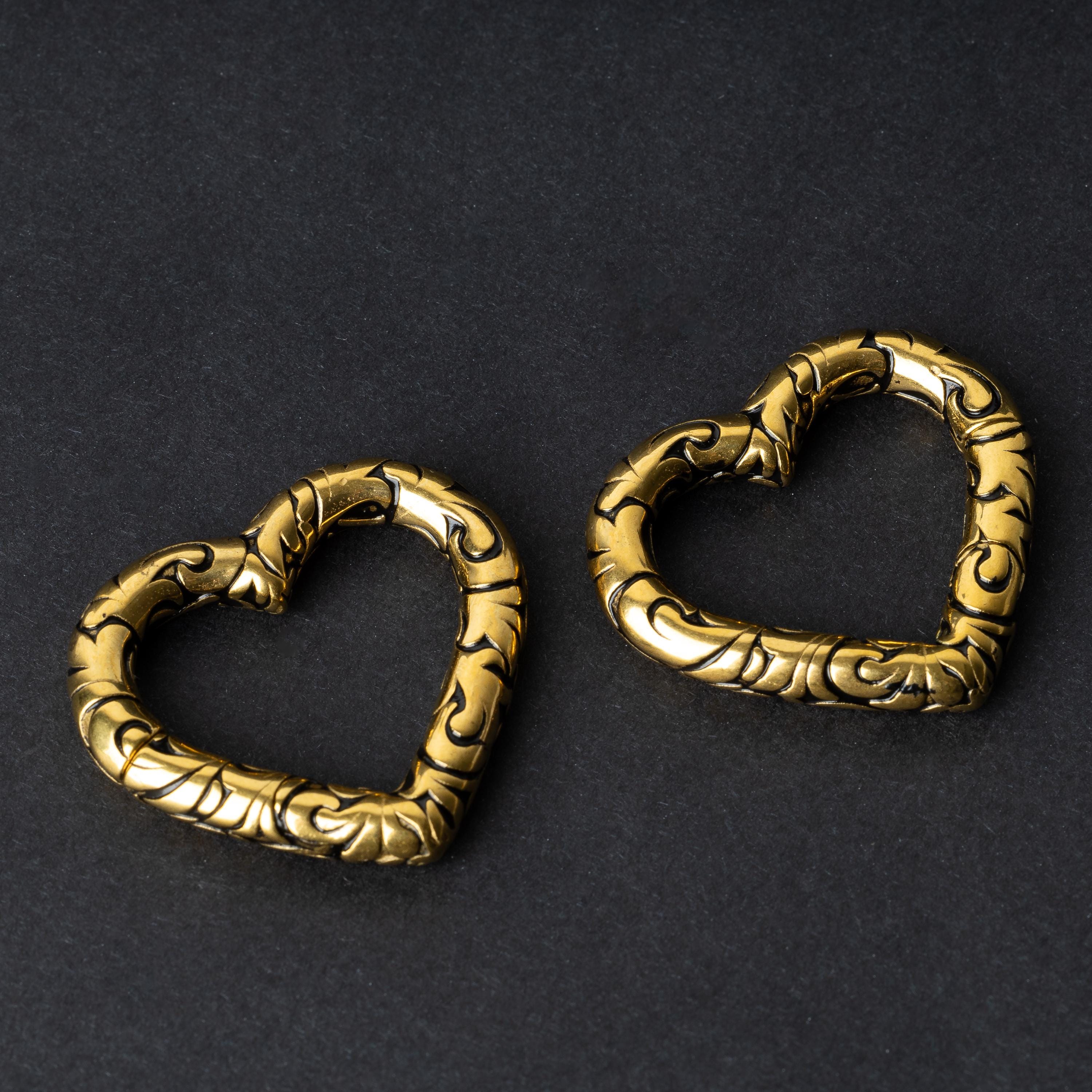 Two heart-shaped engraved saddle plugs in gold on a dark background.