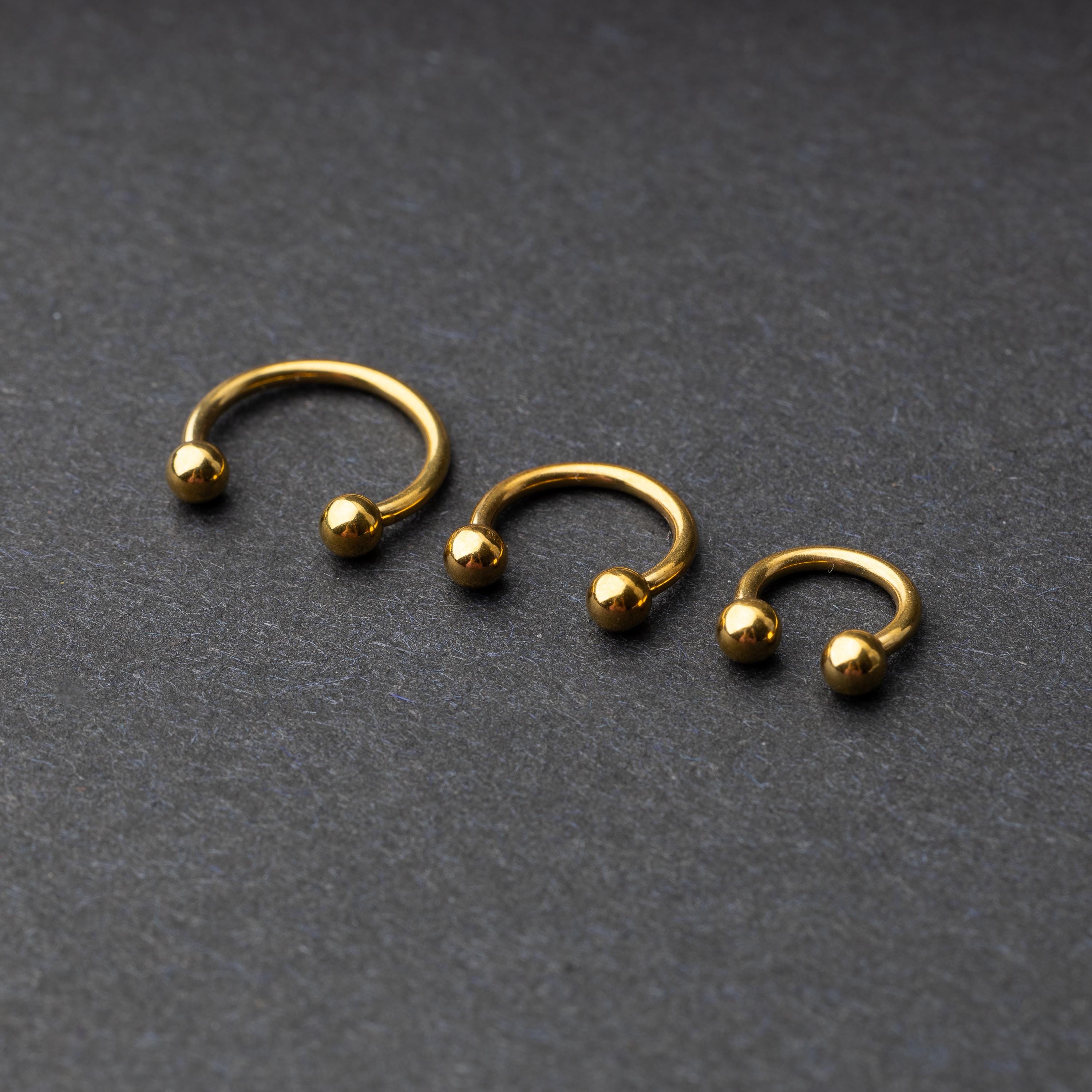 Gold horseshoe rings in three different sizes with ball ends, displayed on a dark background.