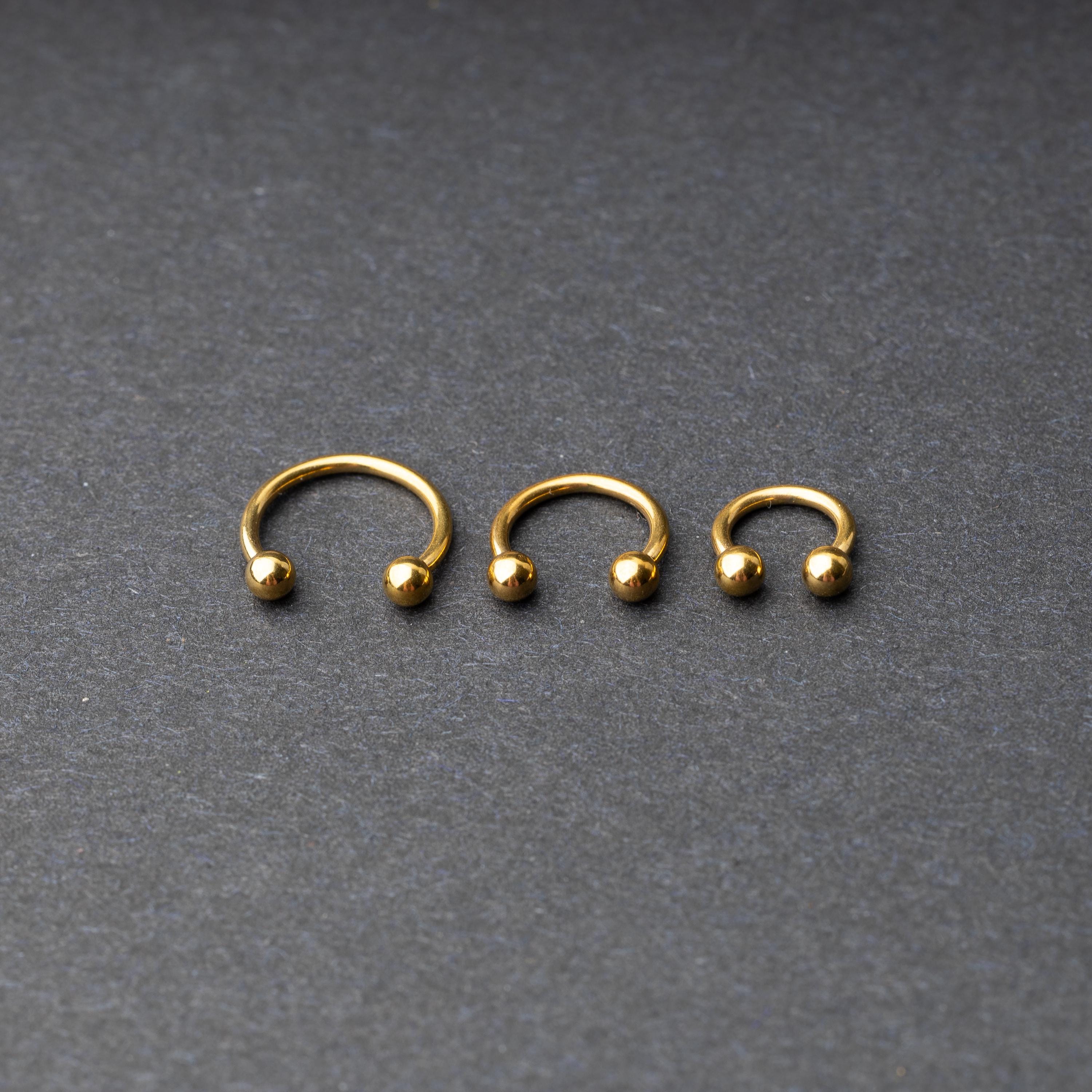 Gold horseshoe rings in three different sizes with ball ends, displayed on a dark background.