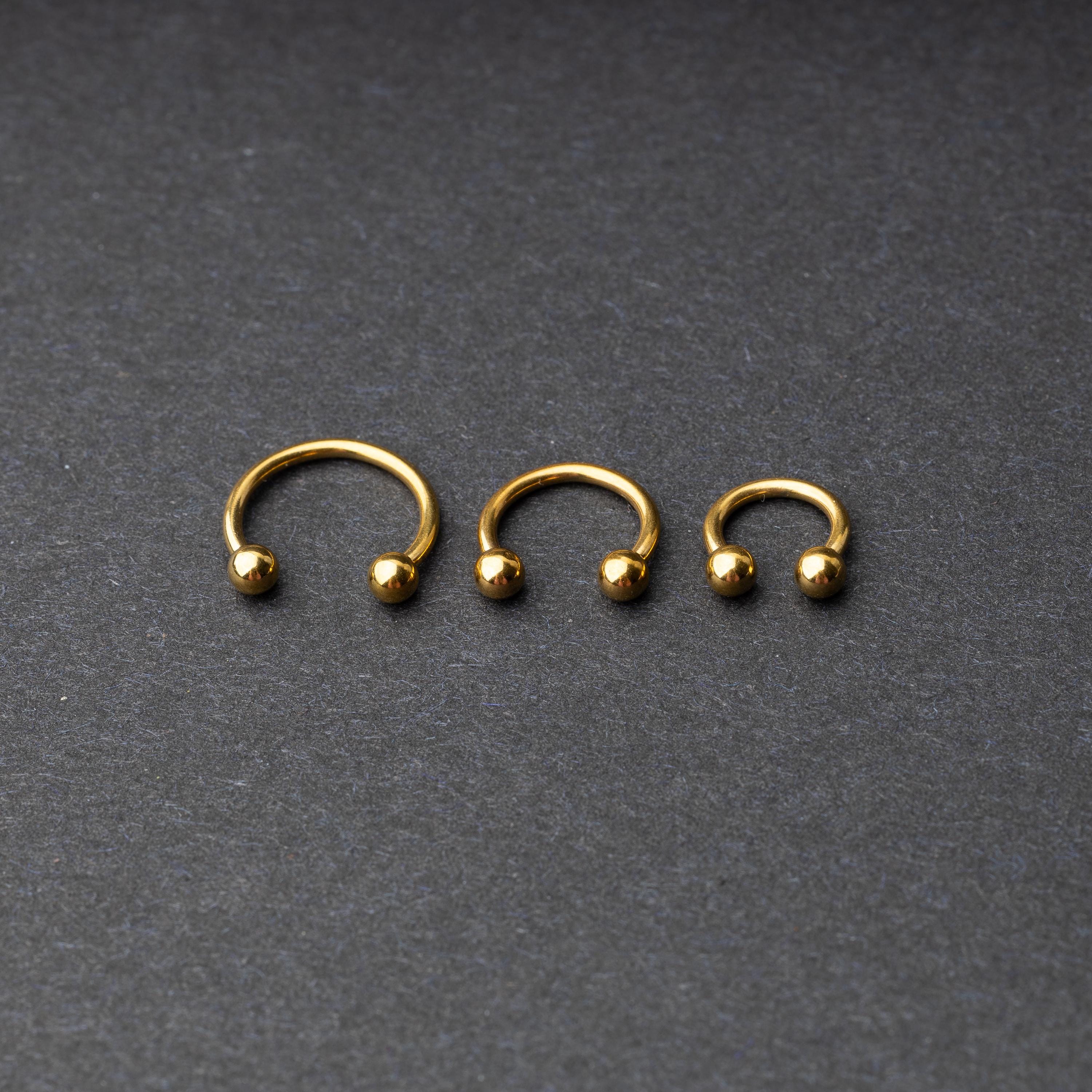 Gold horseshoe rings in three different sizes with ball ends, displayed on a dark background.