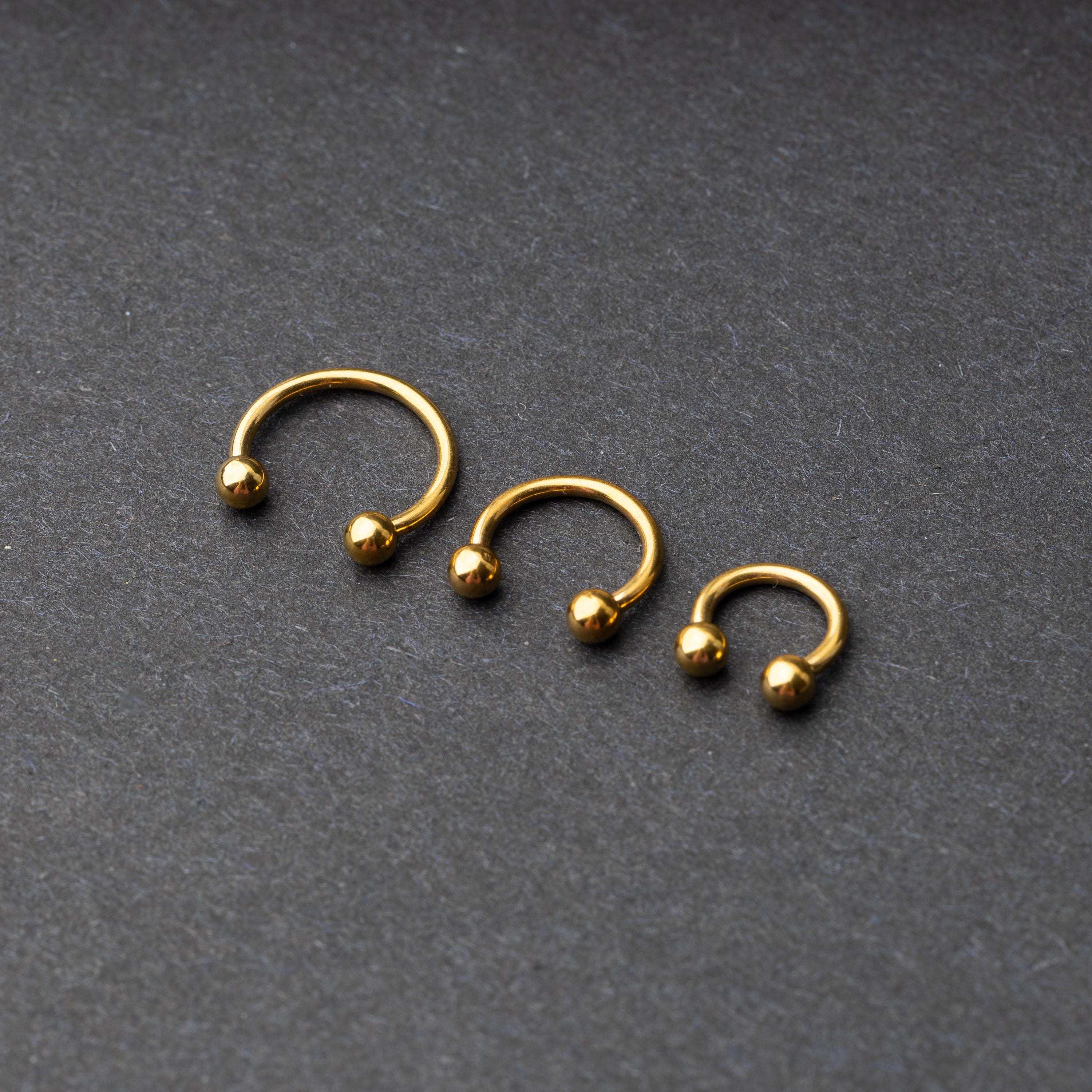 Gold horseshoe rings in three different sizes with ball ends, displayed on a dark background.