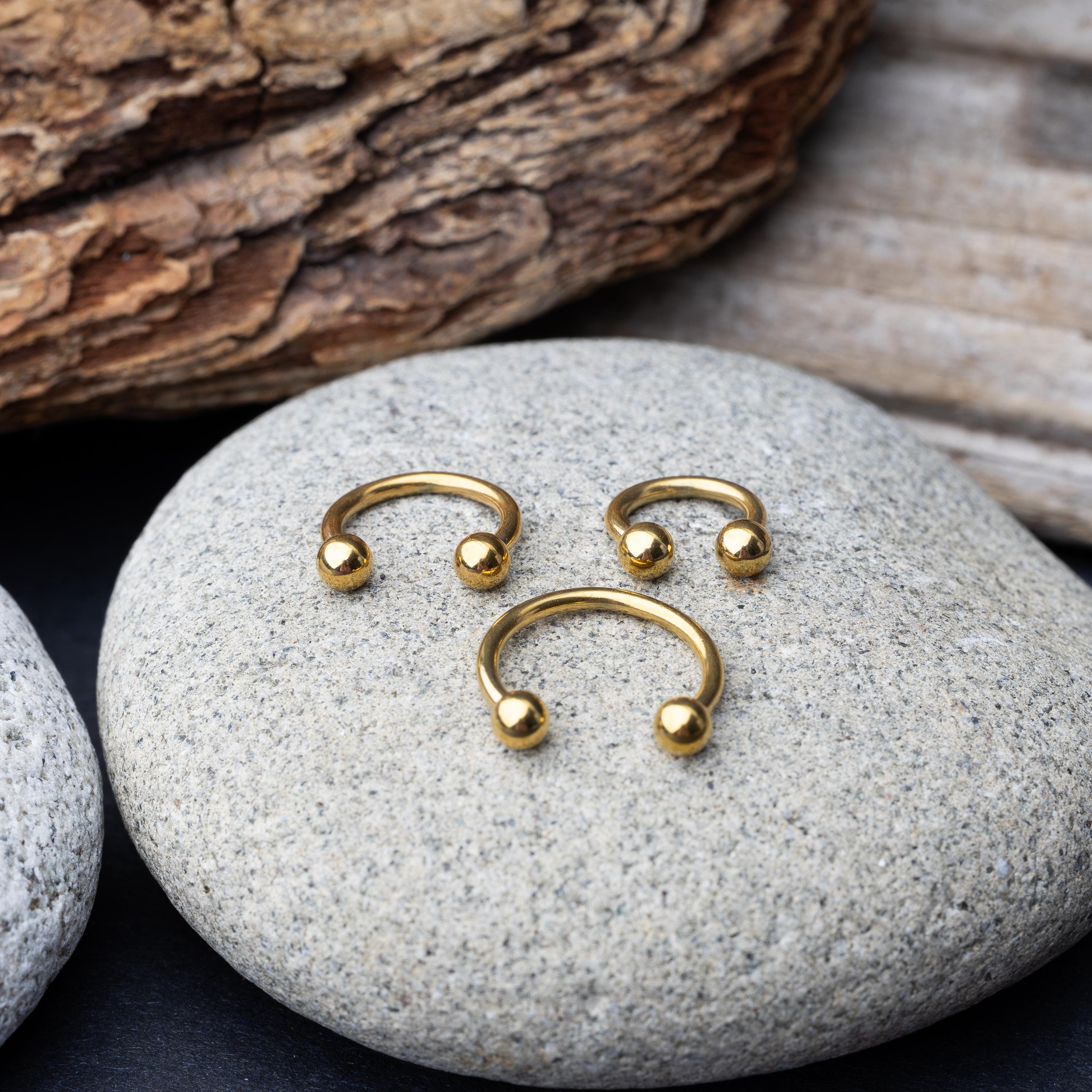 Gold horseshoe rings in three different sizes with ball ends, displayed on a rock.