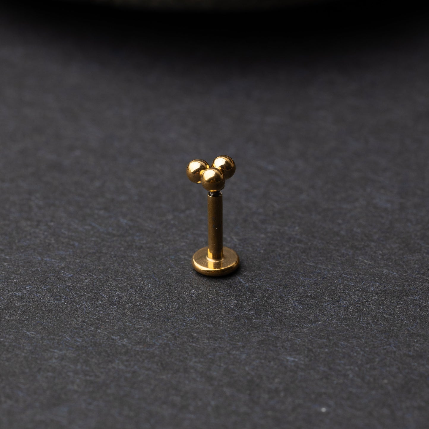 Close-up of three minimalist ball cluster labret studs in a gold finish, displayed on a dark background.
