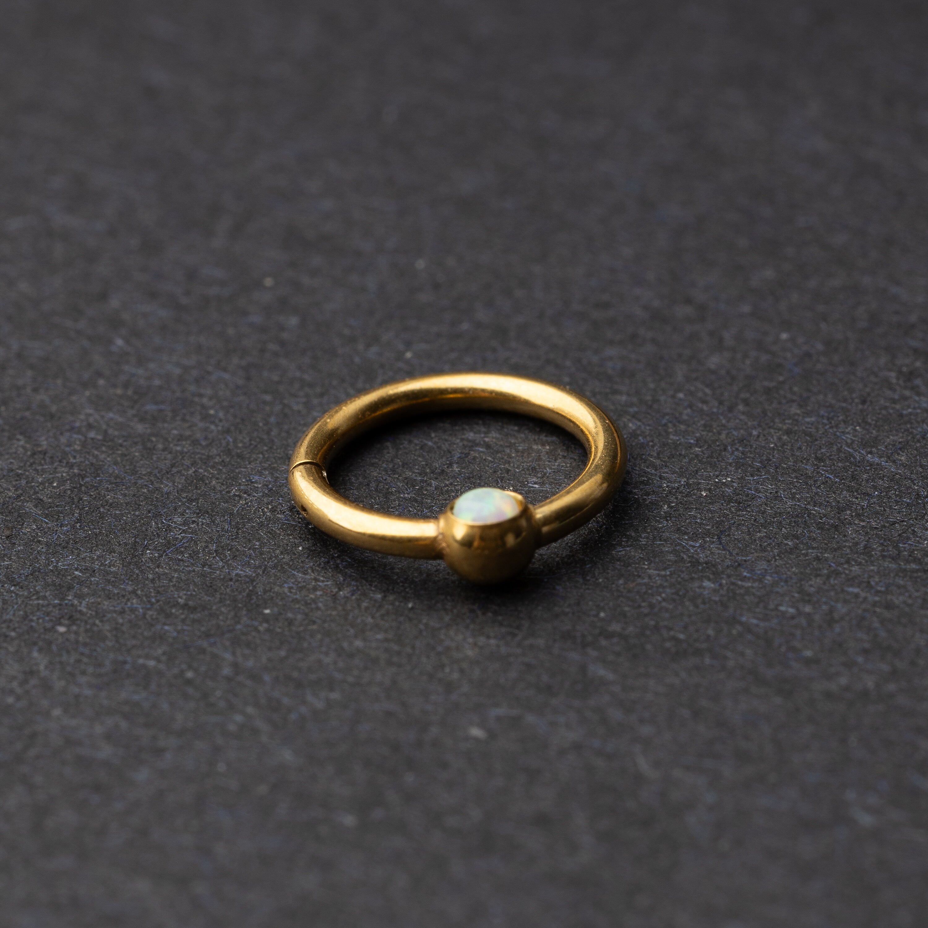 Seamless clicker in gold featuring an opalescent bead, displayed on a dark background.