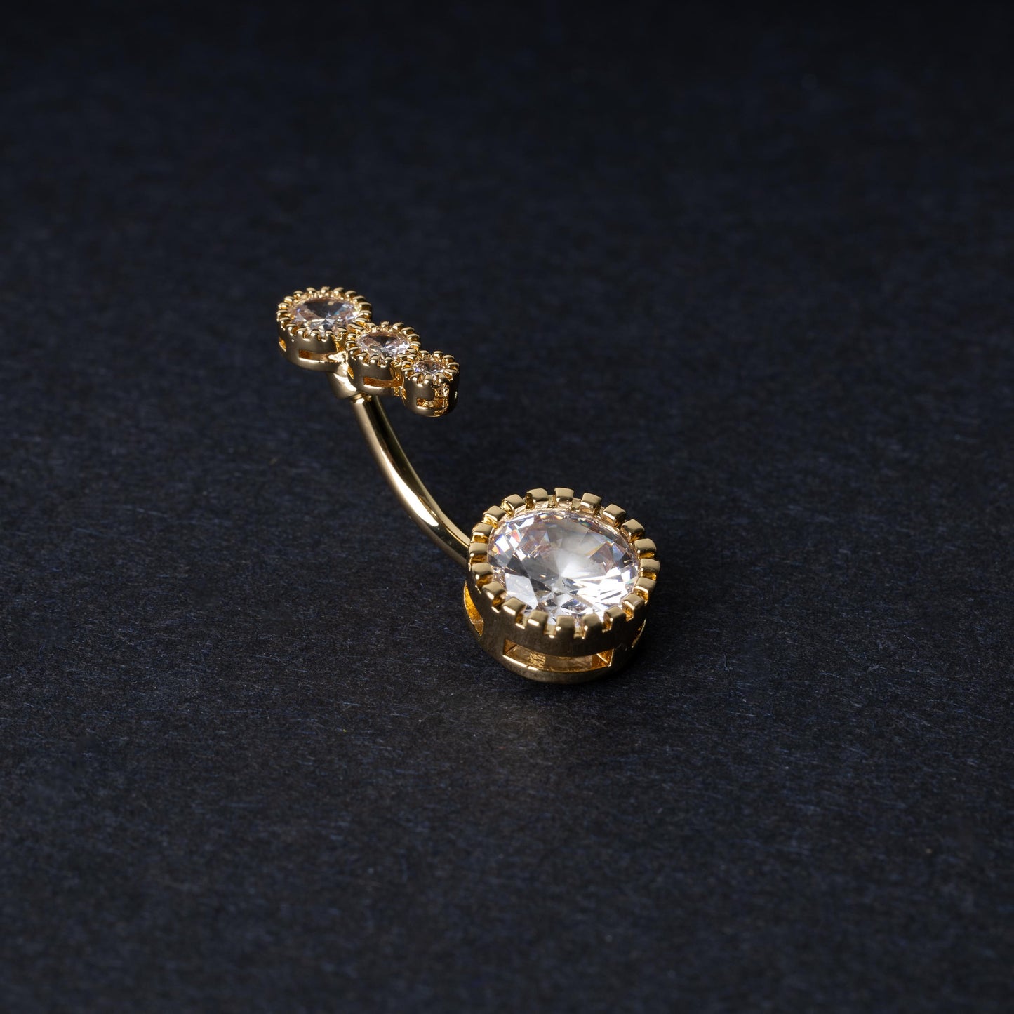 Double-jeweled belly rings in gold with large and small crystal accents, displayed on a dark background.