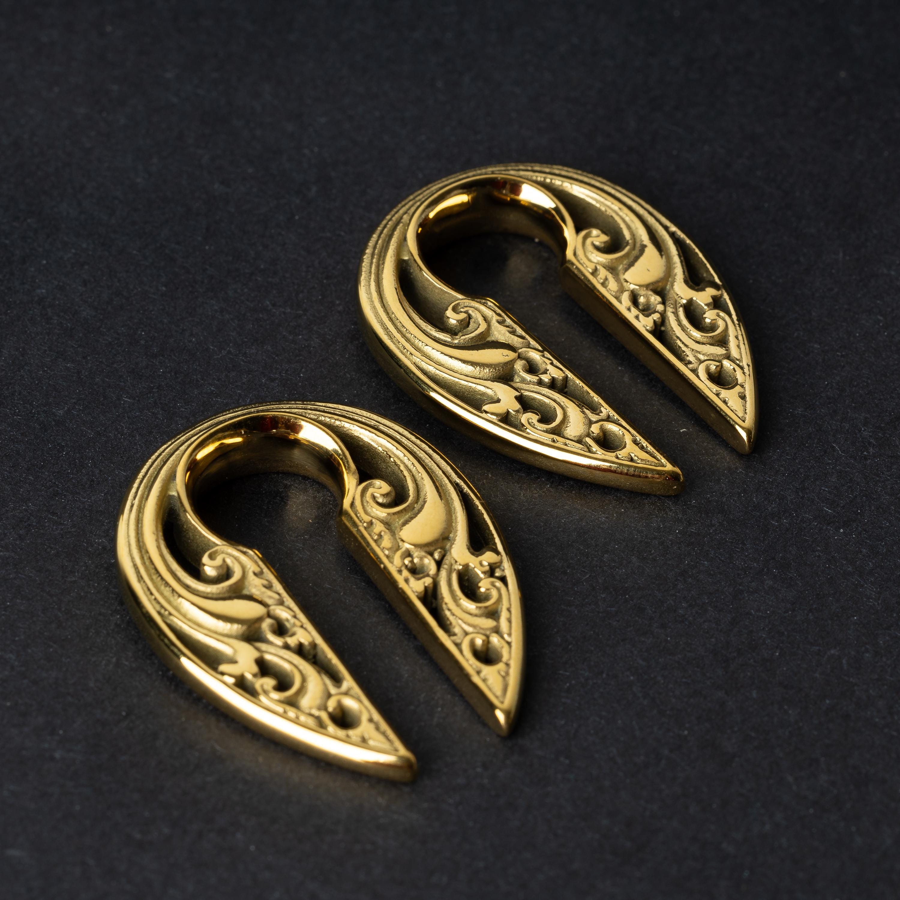 Two split ear weights with intricate filigree detailing, in polished gold, displayed on a dark background.