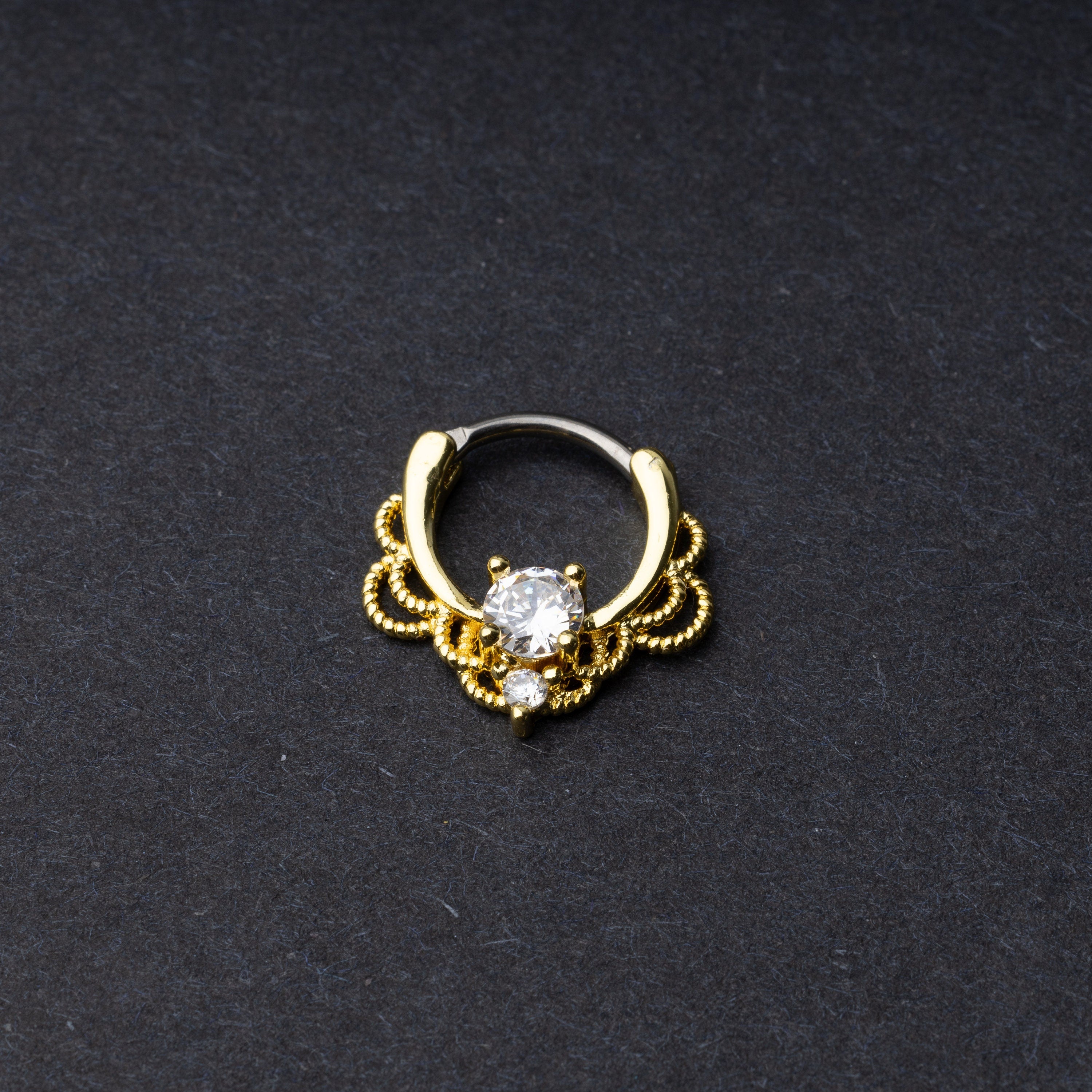 Gold Ornate Septum Ring with a clear gem on a dark background