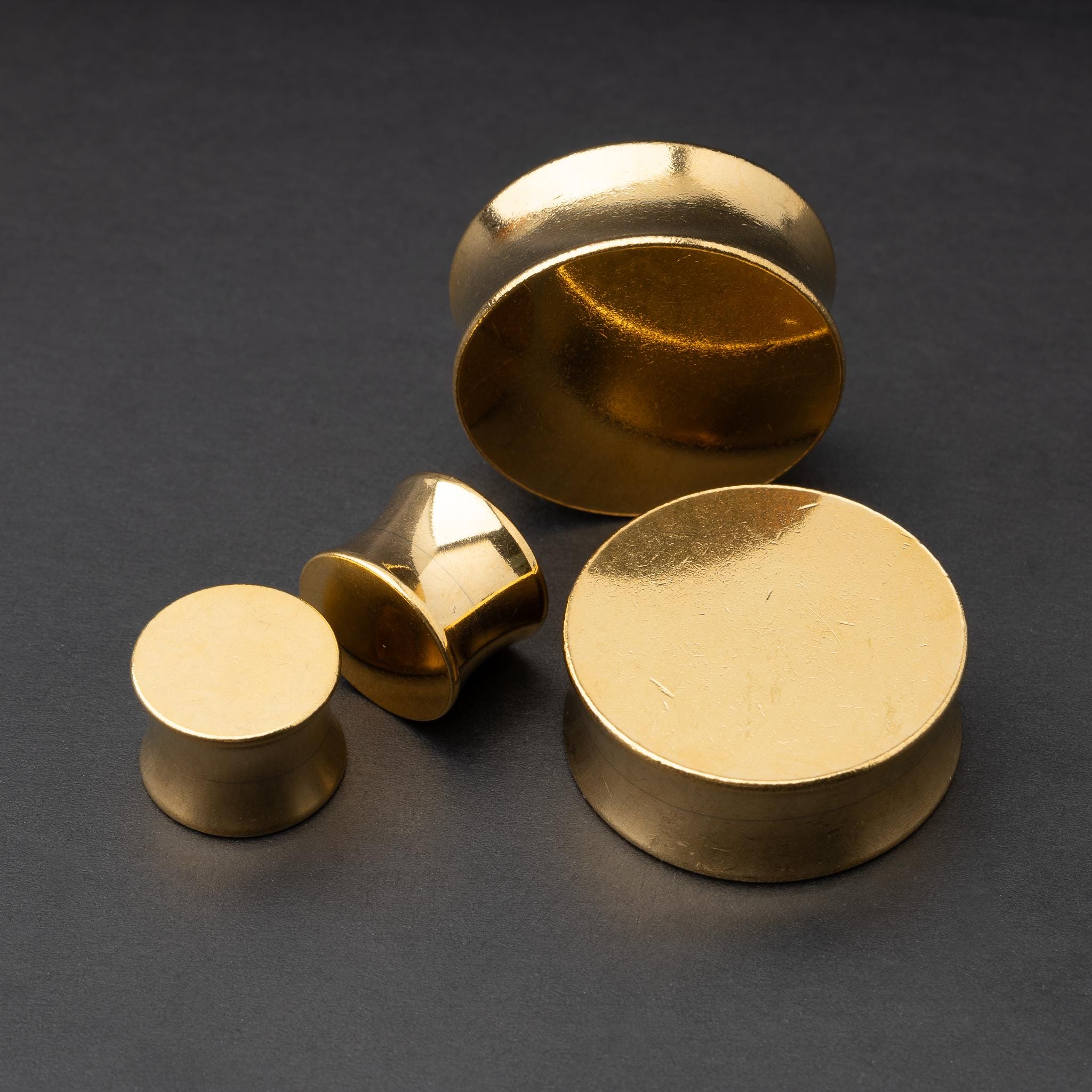 Polished gold plugs in varying sizes, displayed on a dark background.