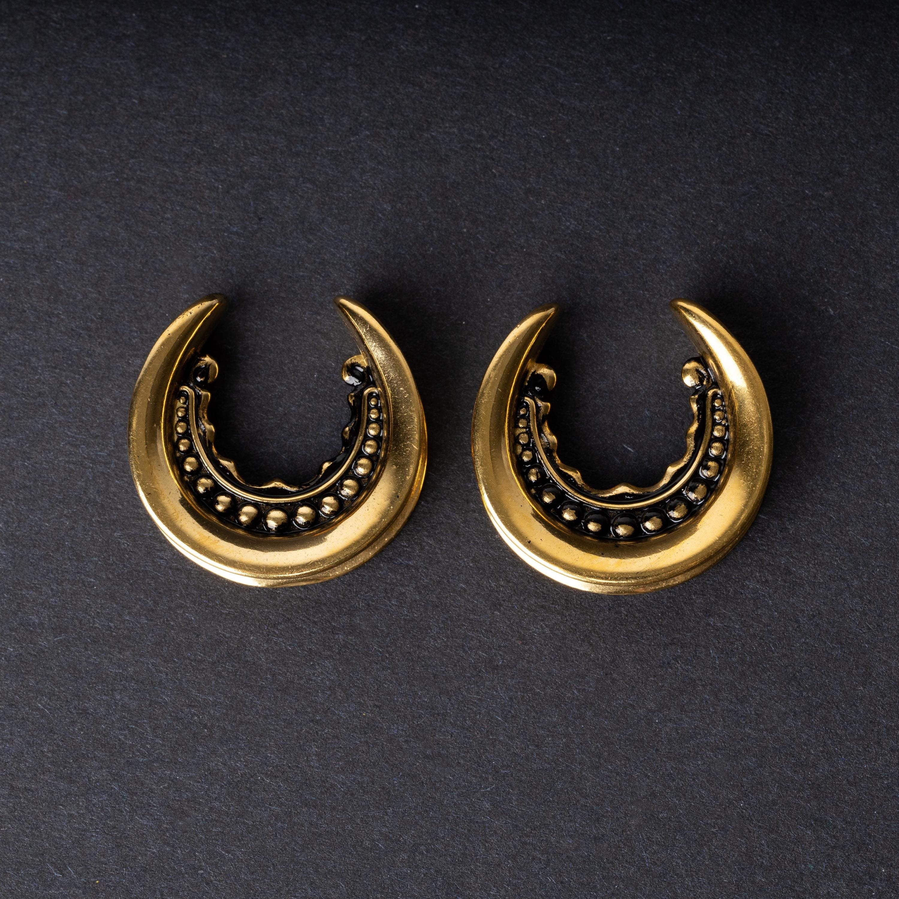Gold crescent-shaped earrings with detailed accents, displayed on a dark background.
