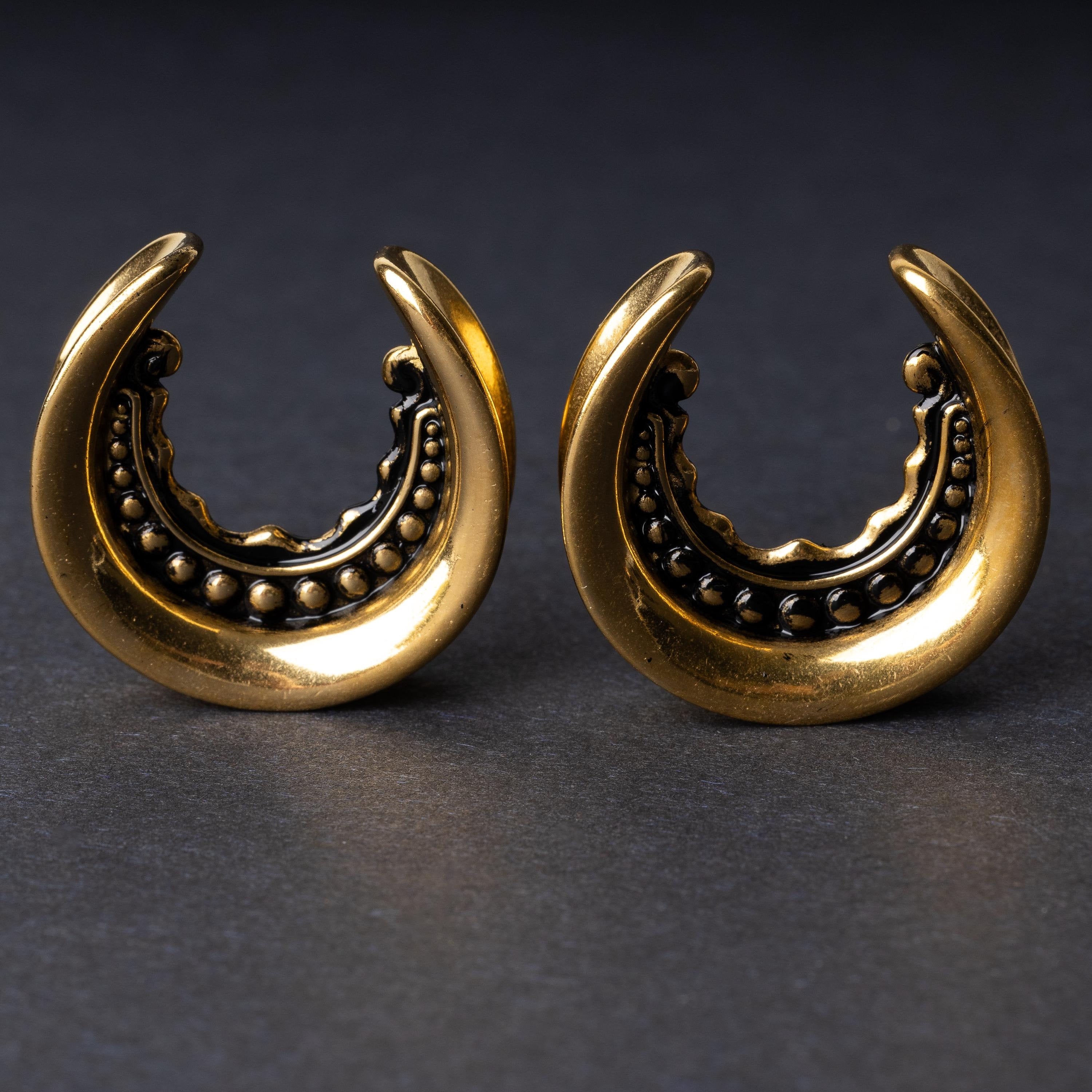 Gold crescent-shaped earrings with detailed accents, displayed on a dark background
