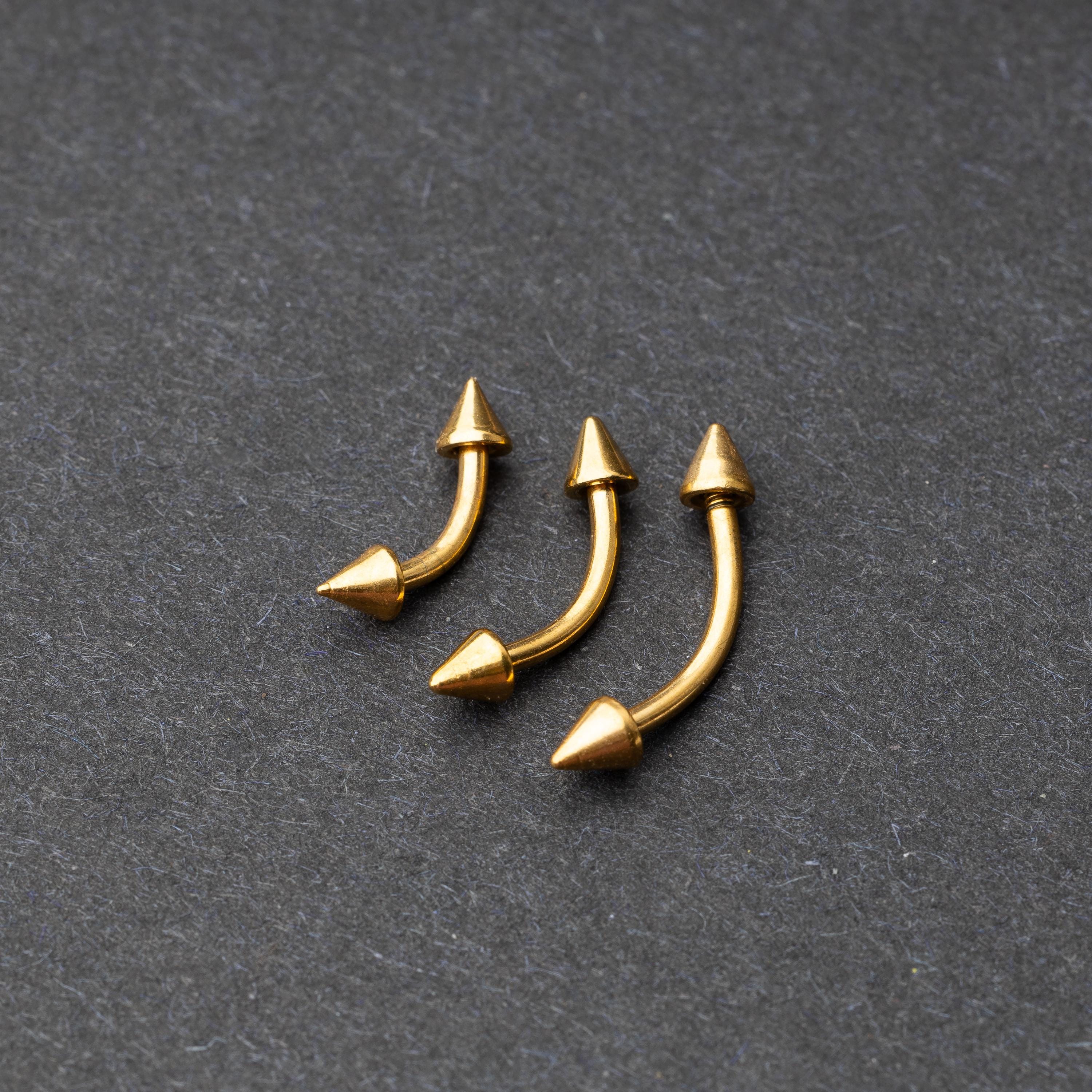 Gold curved barbells with pointed spike ends, displayed on a dark background.