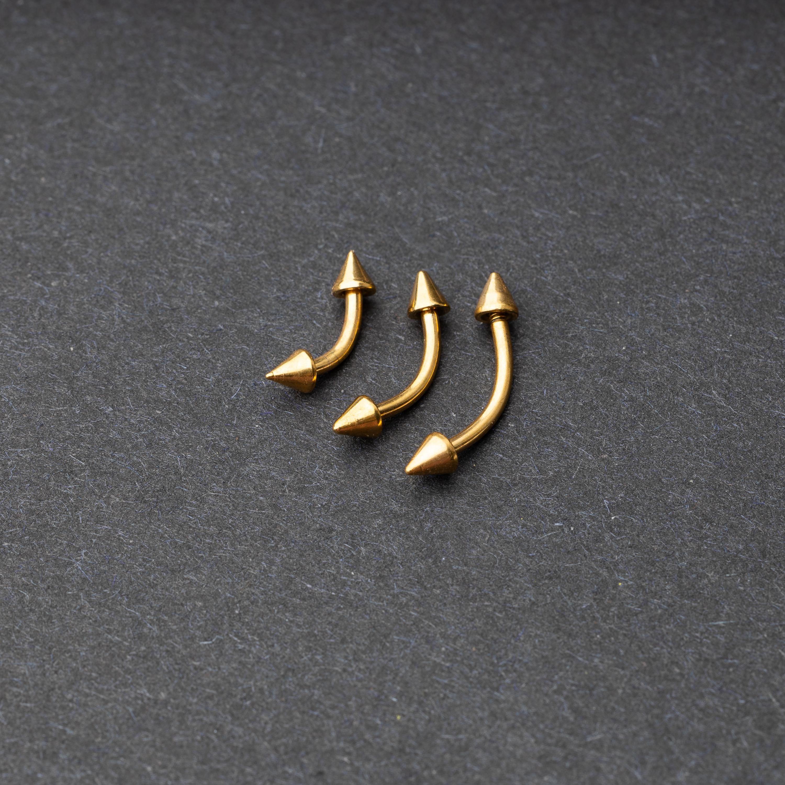 Gold curved barbells with pointed spike ends, displayed on a dark background.