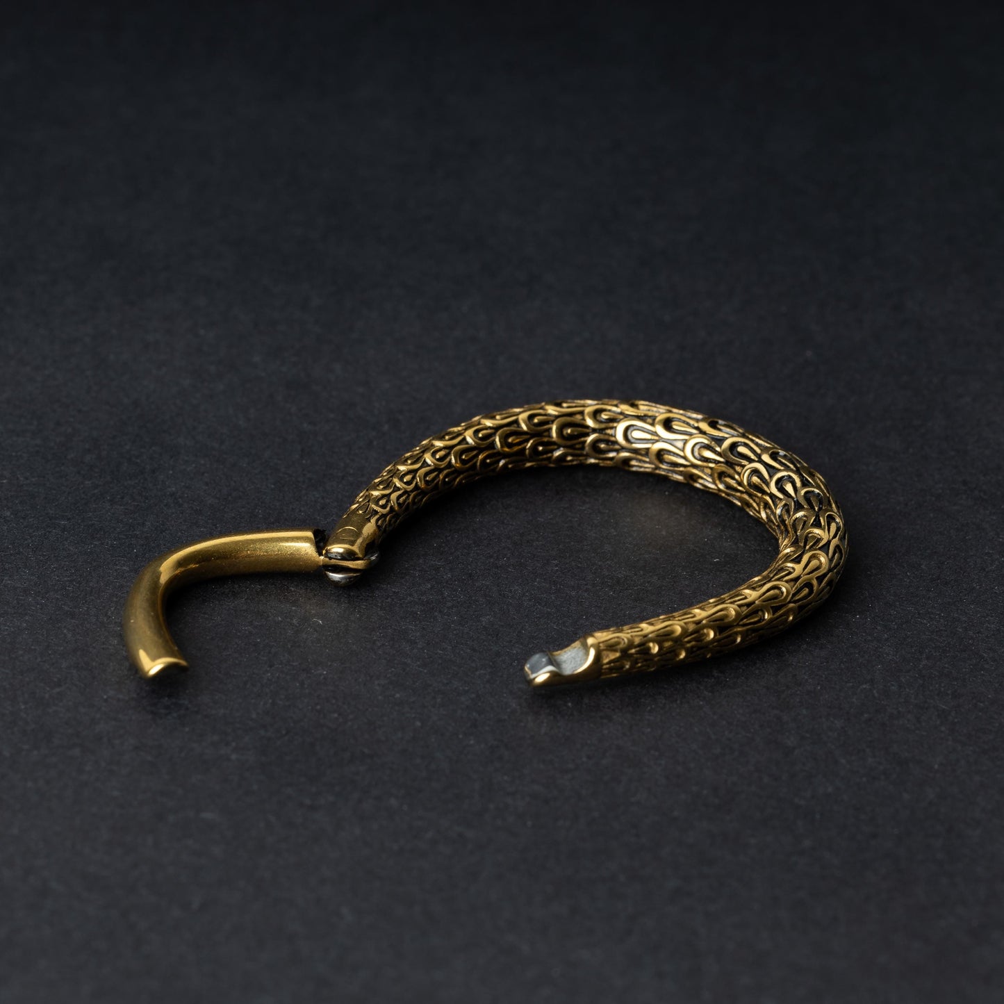 A Gold teardrop ear weight featuring a detailed dragon-scale texture and a seamless hinge closure, displayed on a dark background.