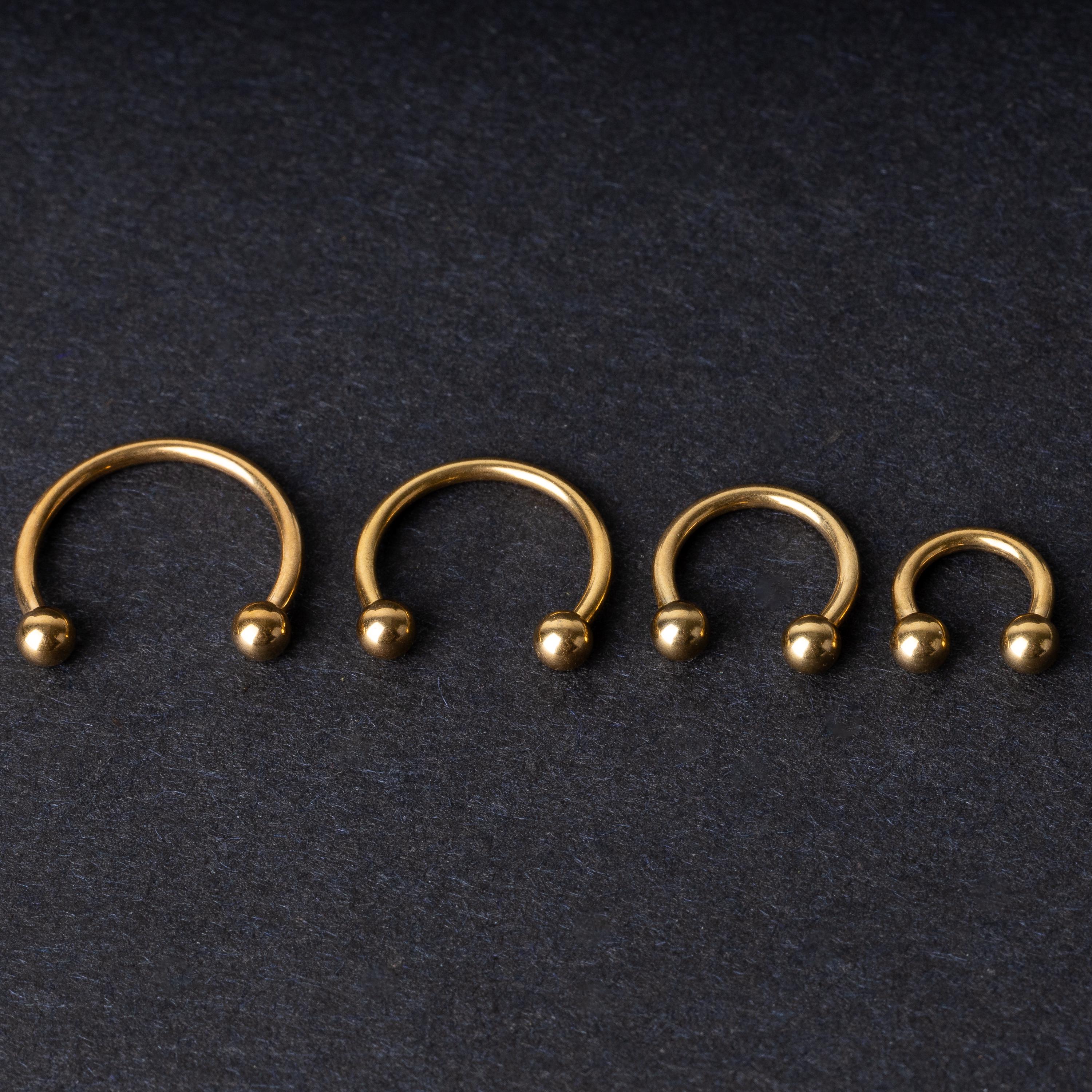 Set of four gold-colored titanium horseshoe rings with ball ends, displayed on a dark textured background.