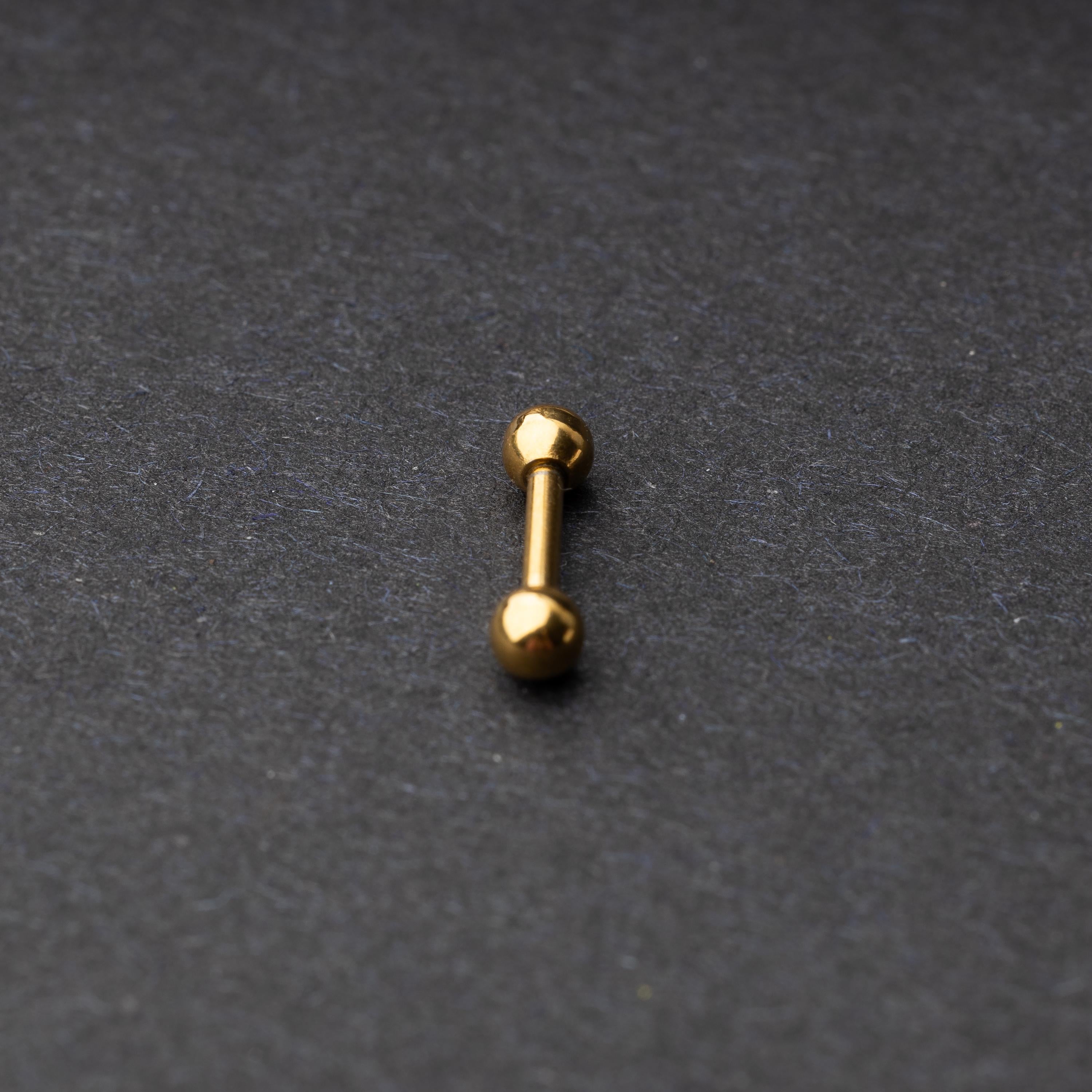 Gold-tone stainless steel barbell with polished spheres on a dark background.