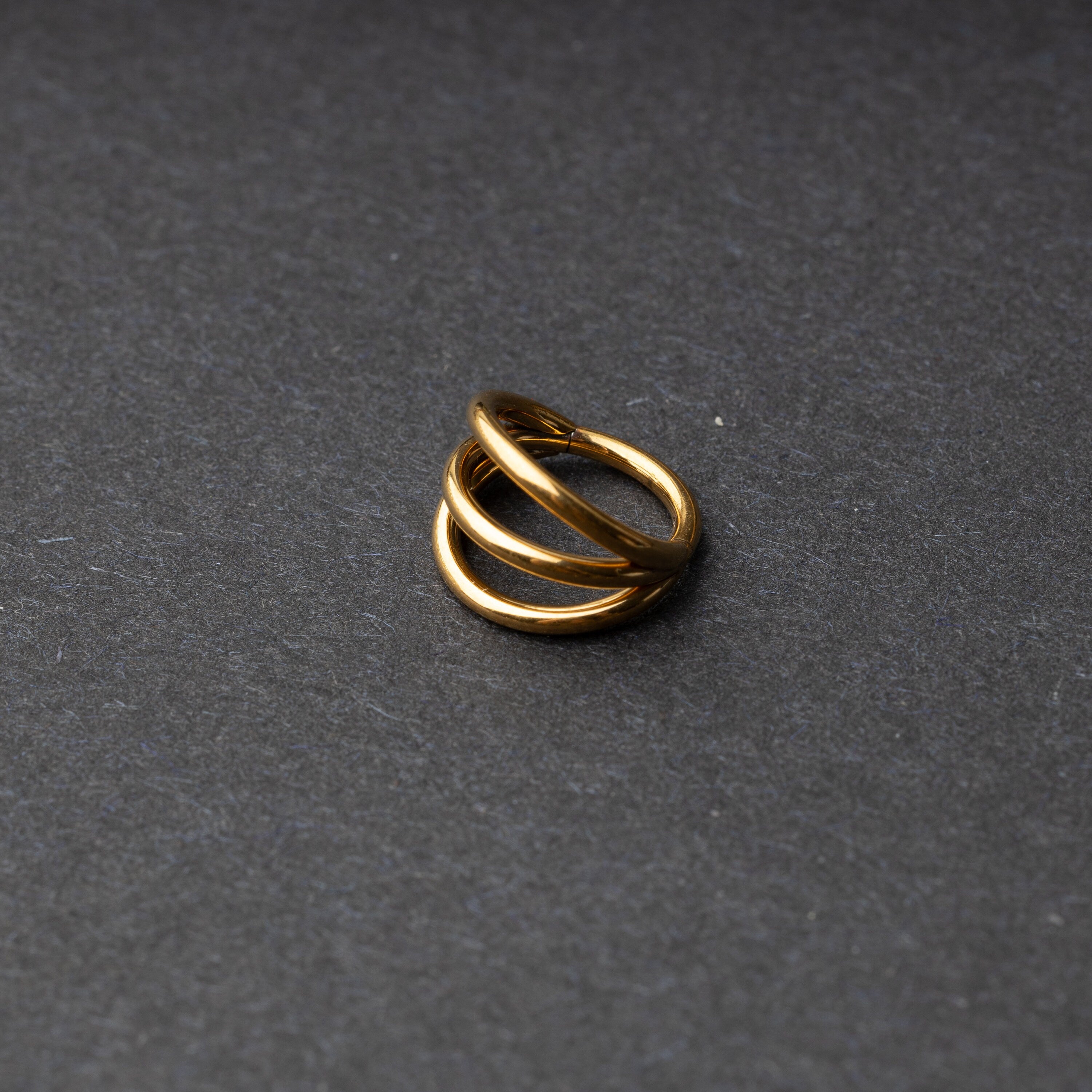 Four triple-band hoop septum clicker ring in gold finish, displayed on a dark background.