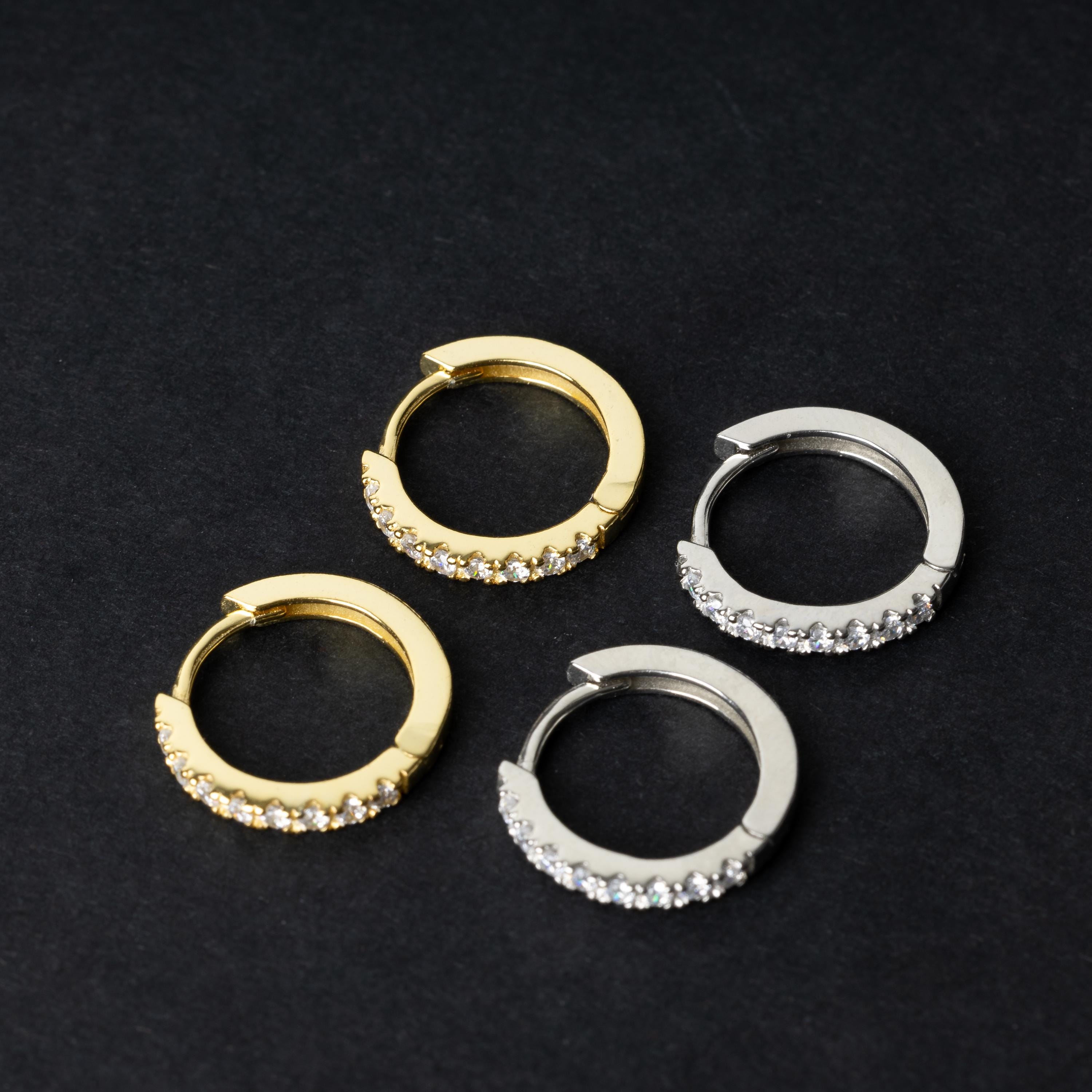 A pair of hoop earrings, one gold and one silver adorned with a row of sparkling cubic zirconia gems, displayed on a black background.
