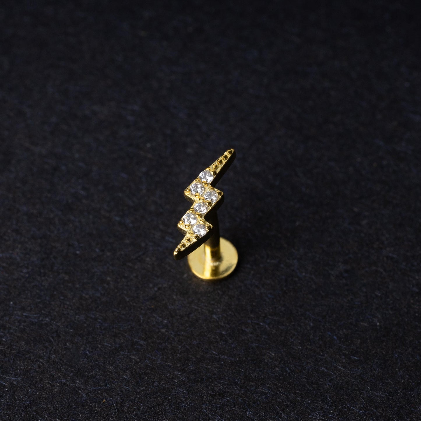 Gold lightning bolt labret stud with crystal detailing, displayed on a dark background.