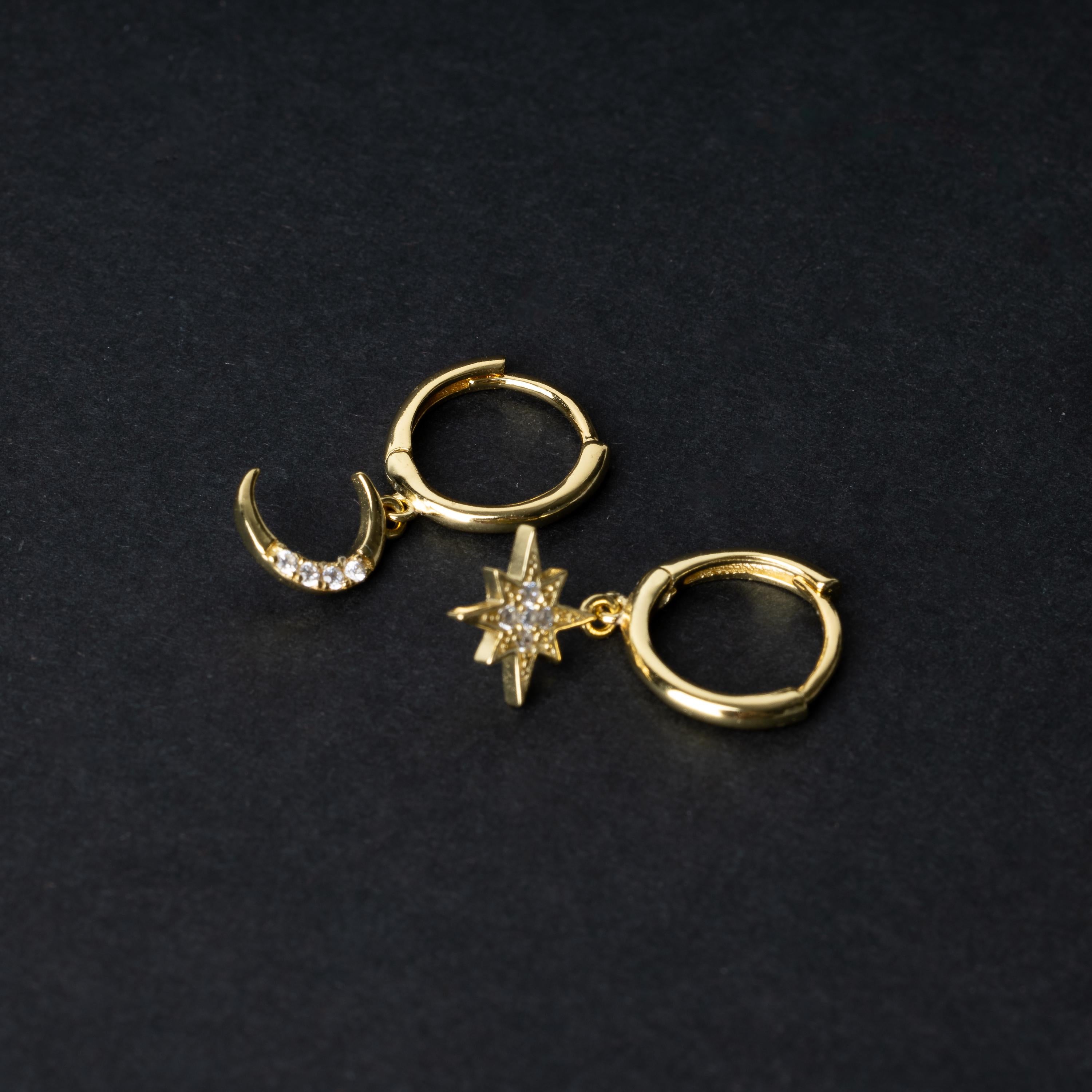 Gold moon and star hoop earrings with cubic zirconia accents, displayed on a dark background.