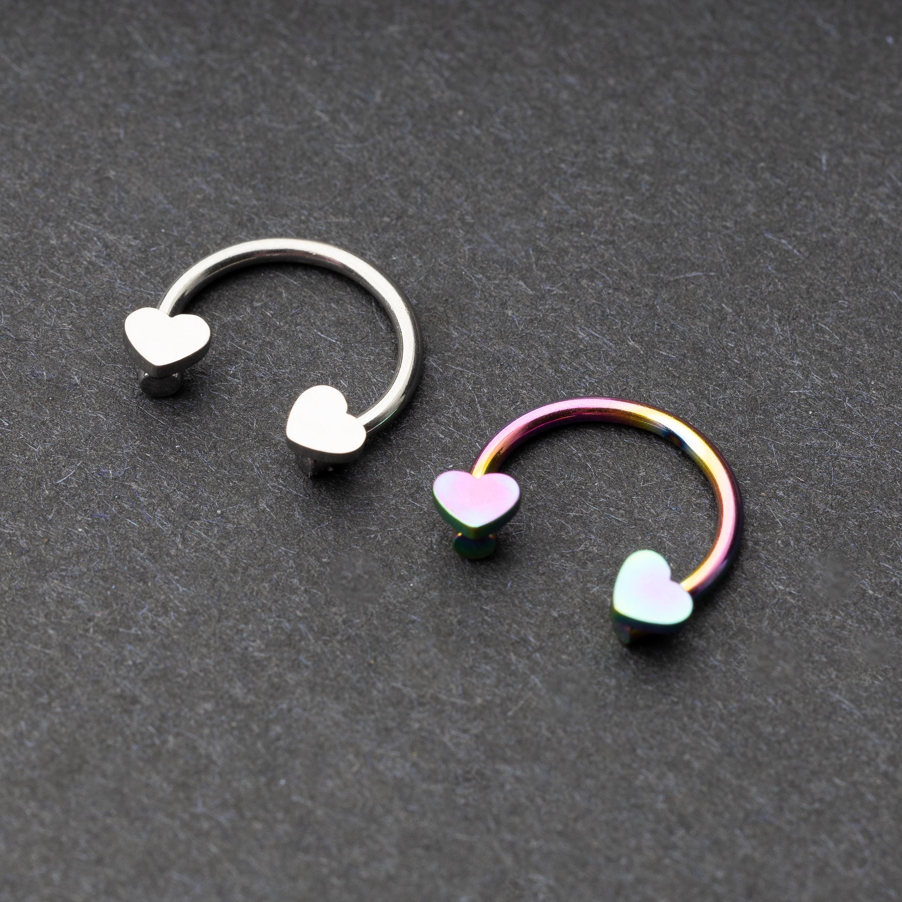 Two horseshoe-shaped hoops with heart-shaped ends in silver and rainbow finishes, displayed on a dark background.