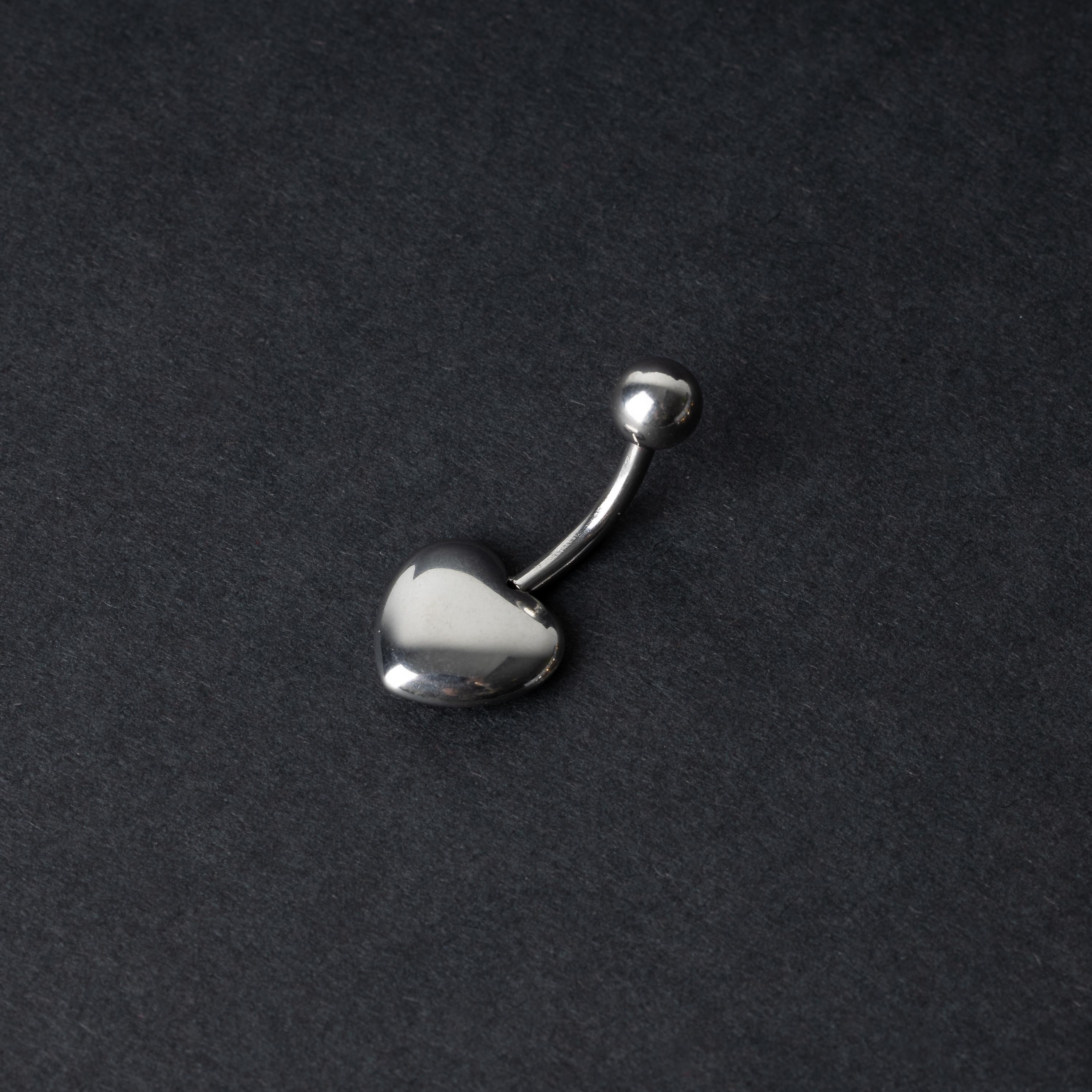 Silver heart shaped belly bar on a dark background