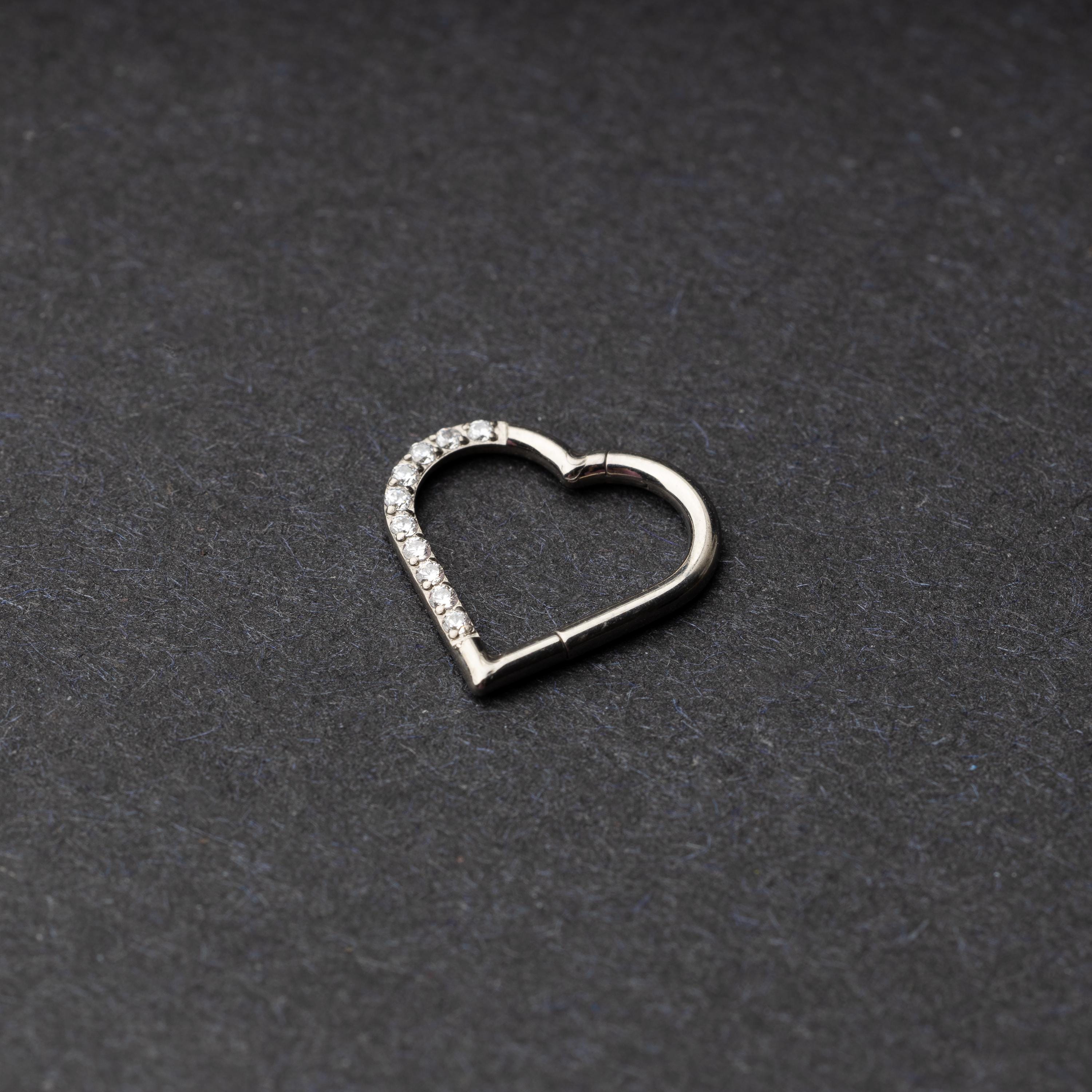 Heart-shaped daith clicker with crystal accents along one side, displayed on a dark textured background.