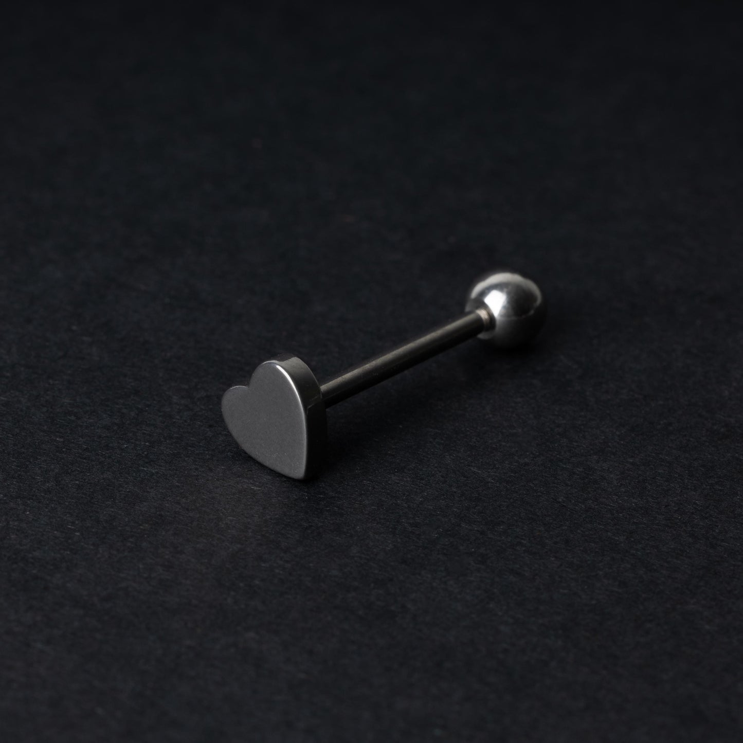 Heart shaped tongue bar in silver, displayed on a dark background.