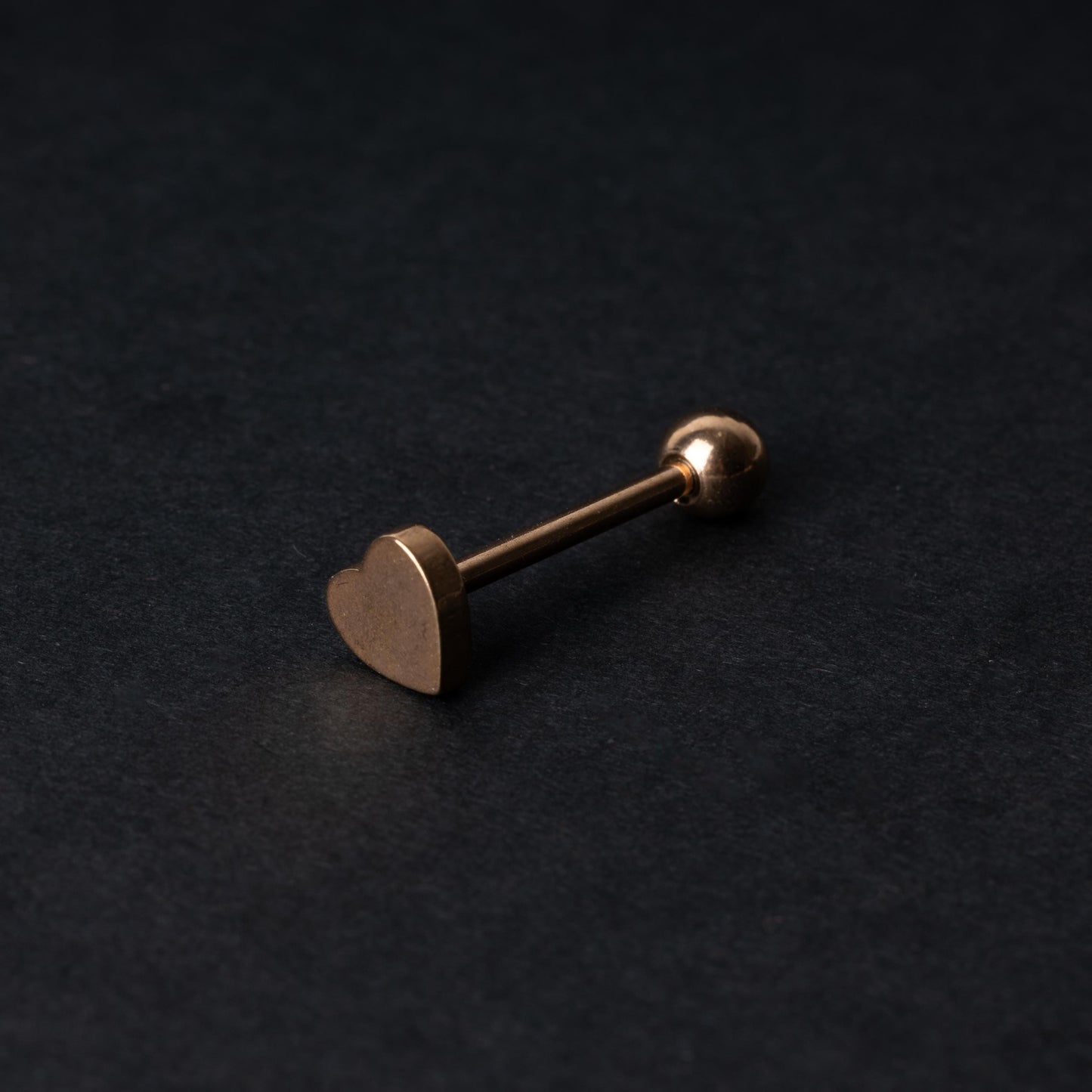Heart shaped tongue bar in rose gold, displayed on a dark background.