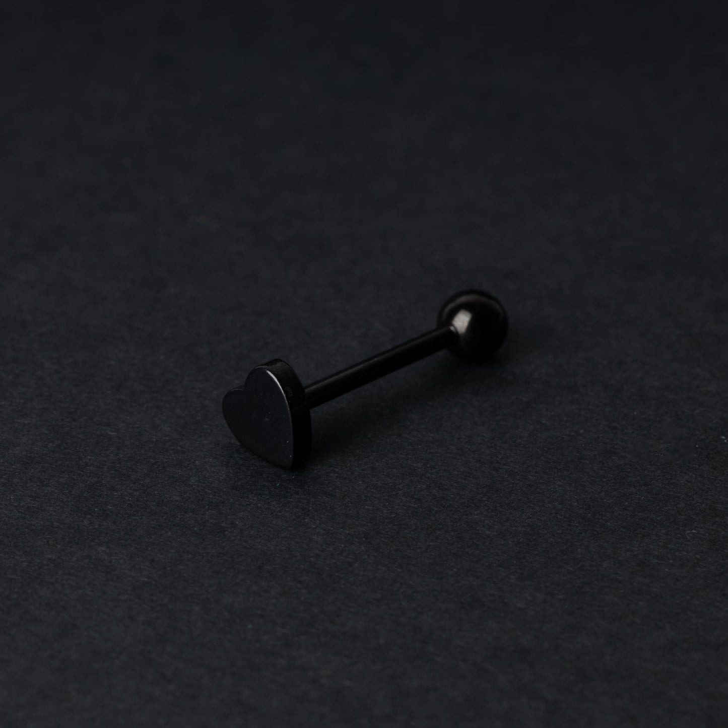 Heart shaped tongue bar in black, displayed on a dark background.