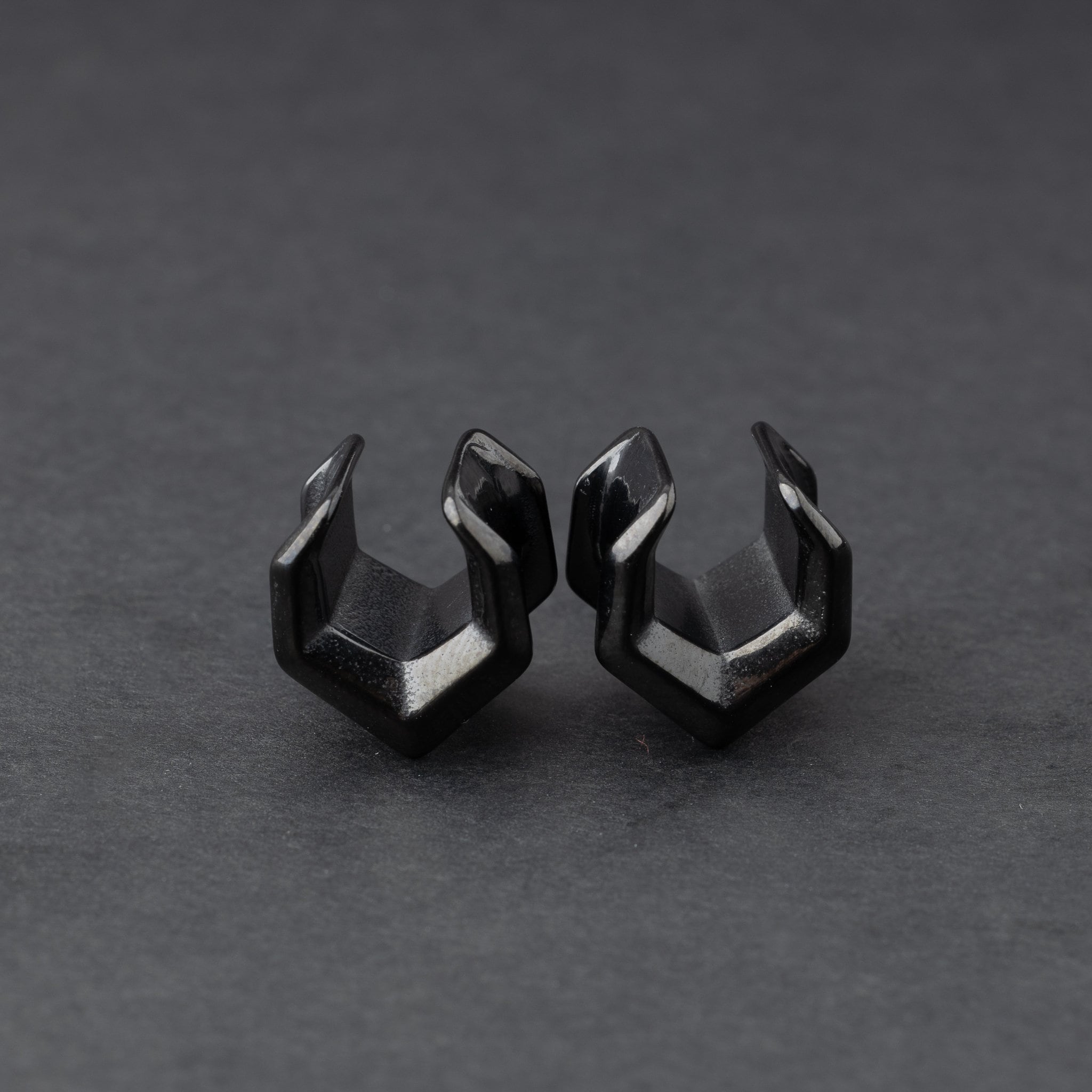 Black geometric chevron-shaped ear cuffs displayed on a dark background.