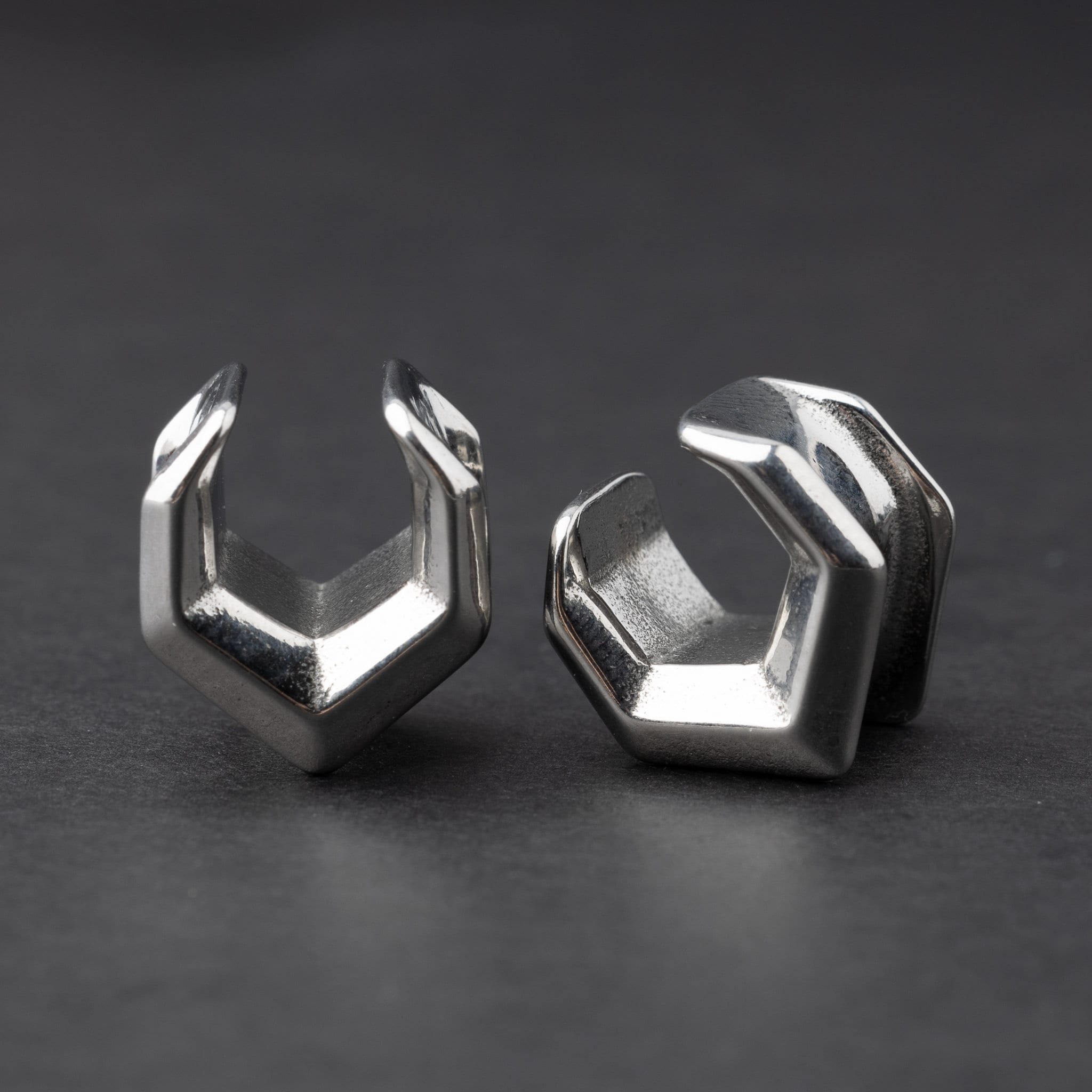 Silver geometric chevron-shaped ear cuffs displayed on a dark background