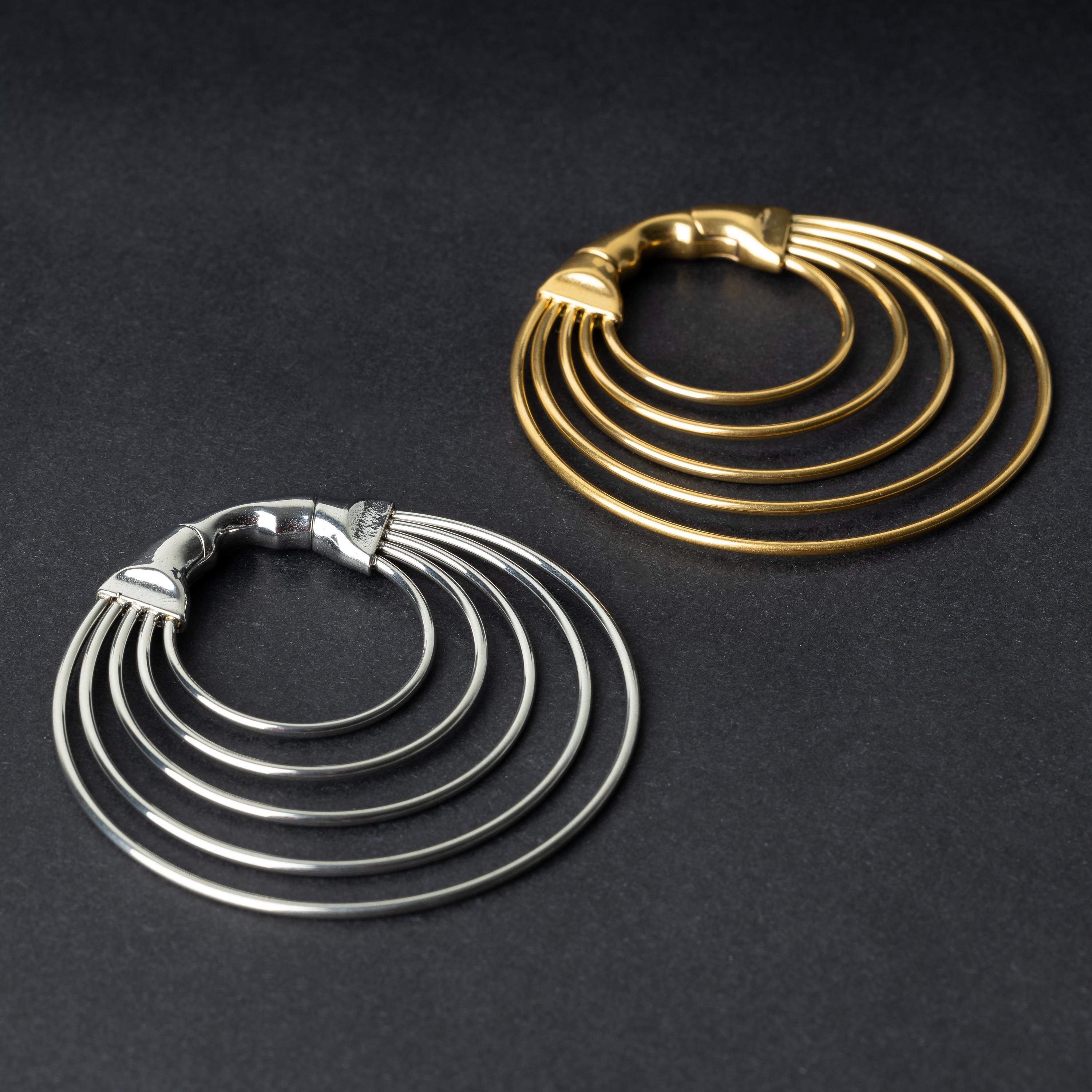 Two multi-hoop ear weights, one in polished silver and the other in polished gold, featuring layered curves and a seamless hinge closure, displayed on a dark background.