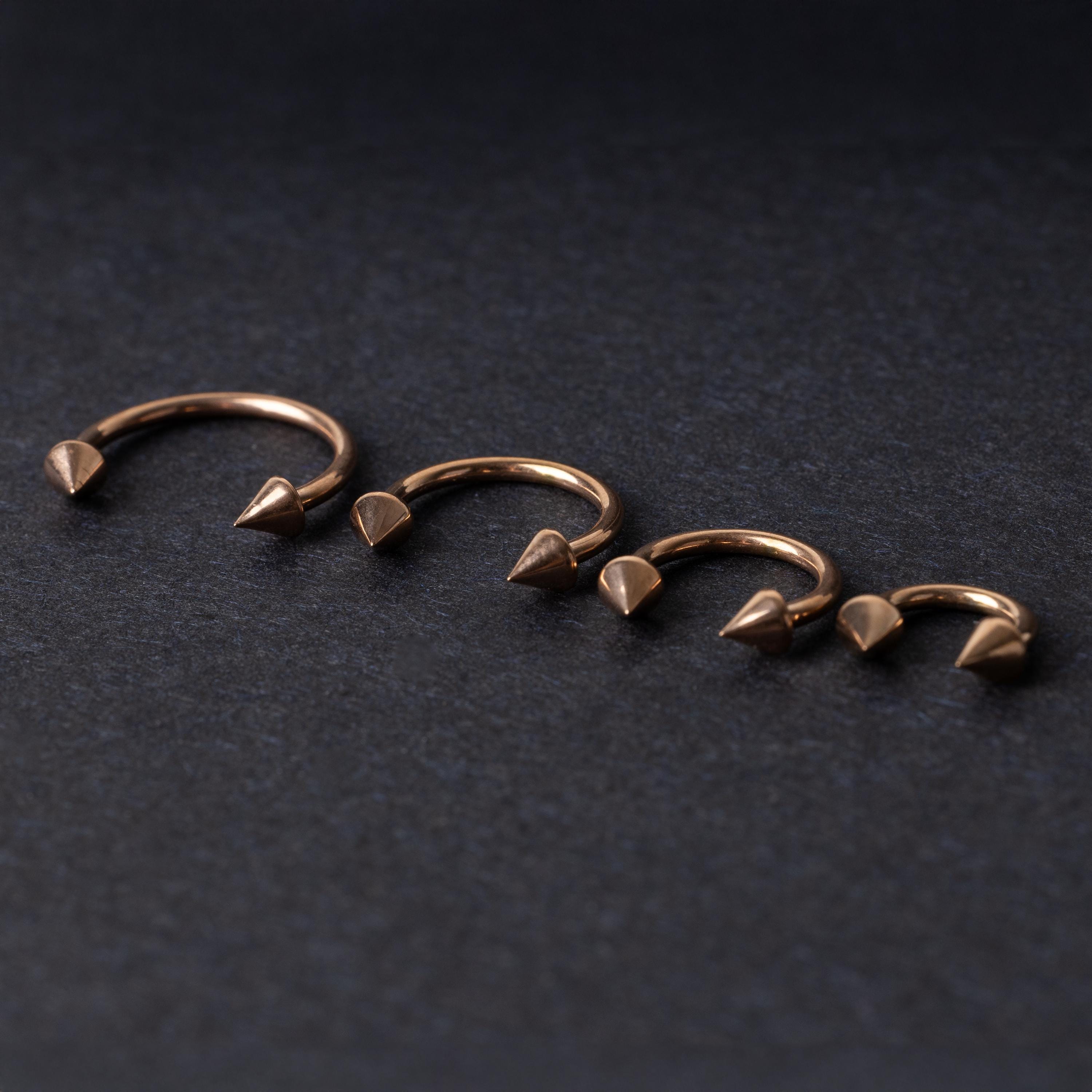 Four rose gold-tone horseshoe hoops with spike ends, arranged in descending size order on a dark textured background.