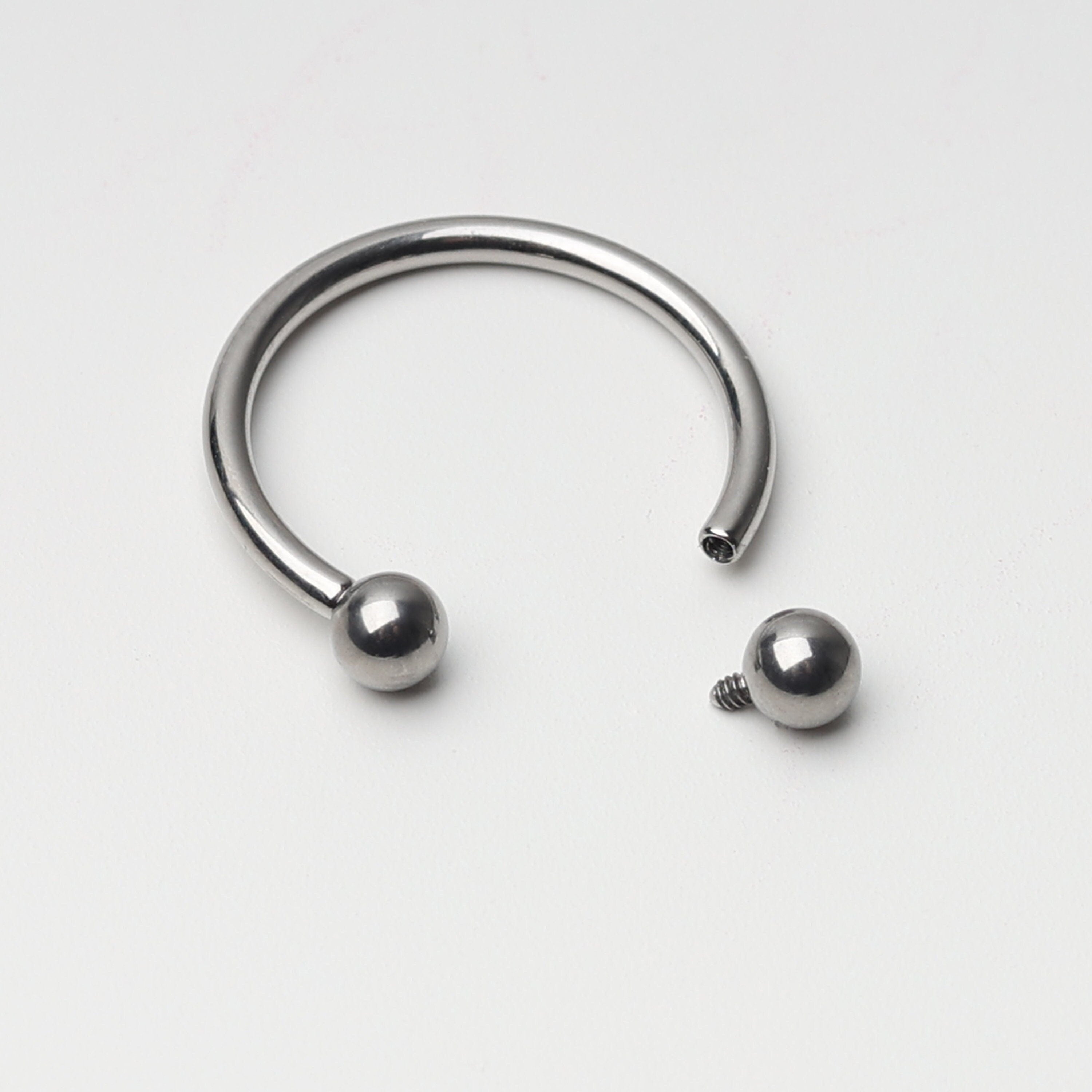 Titanium horseshoe ring with ball ends, displayed on a light background.