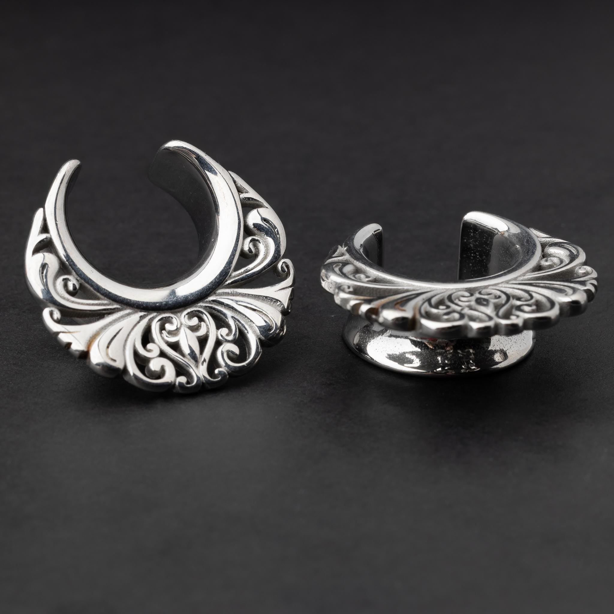 Pair of silver saddle tunnels with swirling decorative patterns for stretched ears.