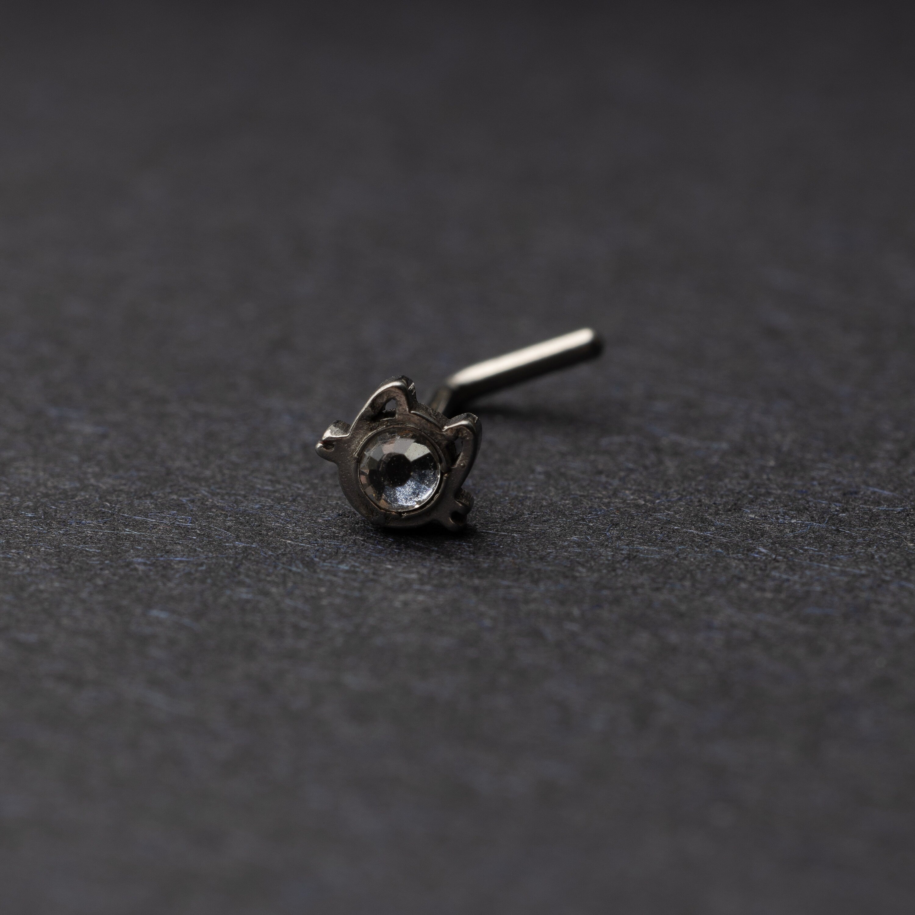 A silver stud earring in the shape of a cat’s face with a bezel-set gemstone, displayed on a dark background.