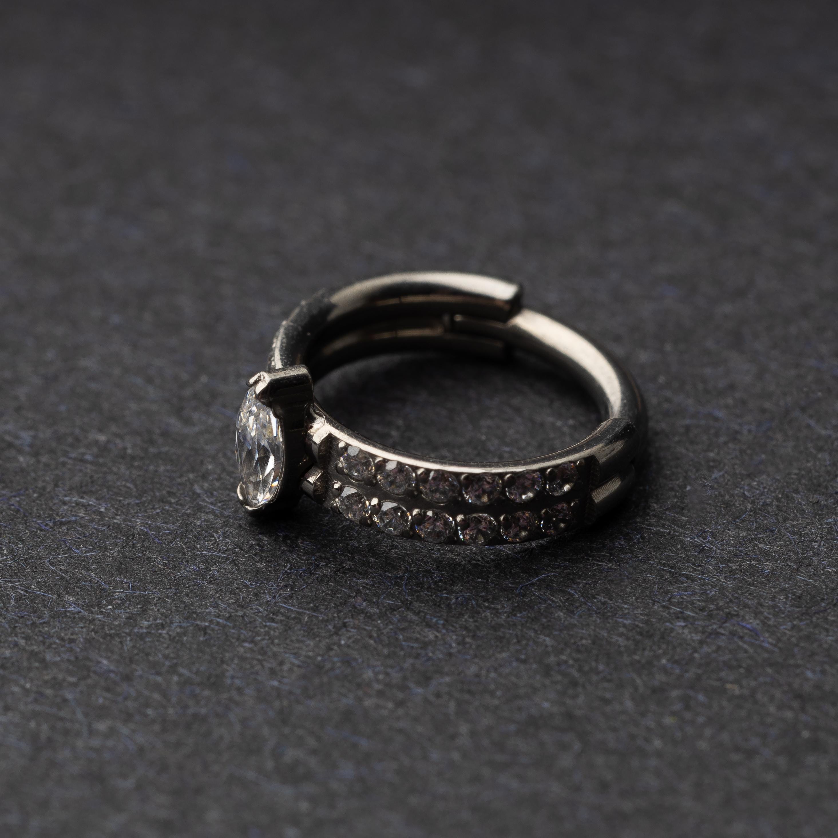 A close-up of a marquise gemstone septum or helix clicker with dual rows of sparkling gems displayed on a dark background.