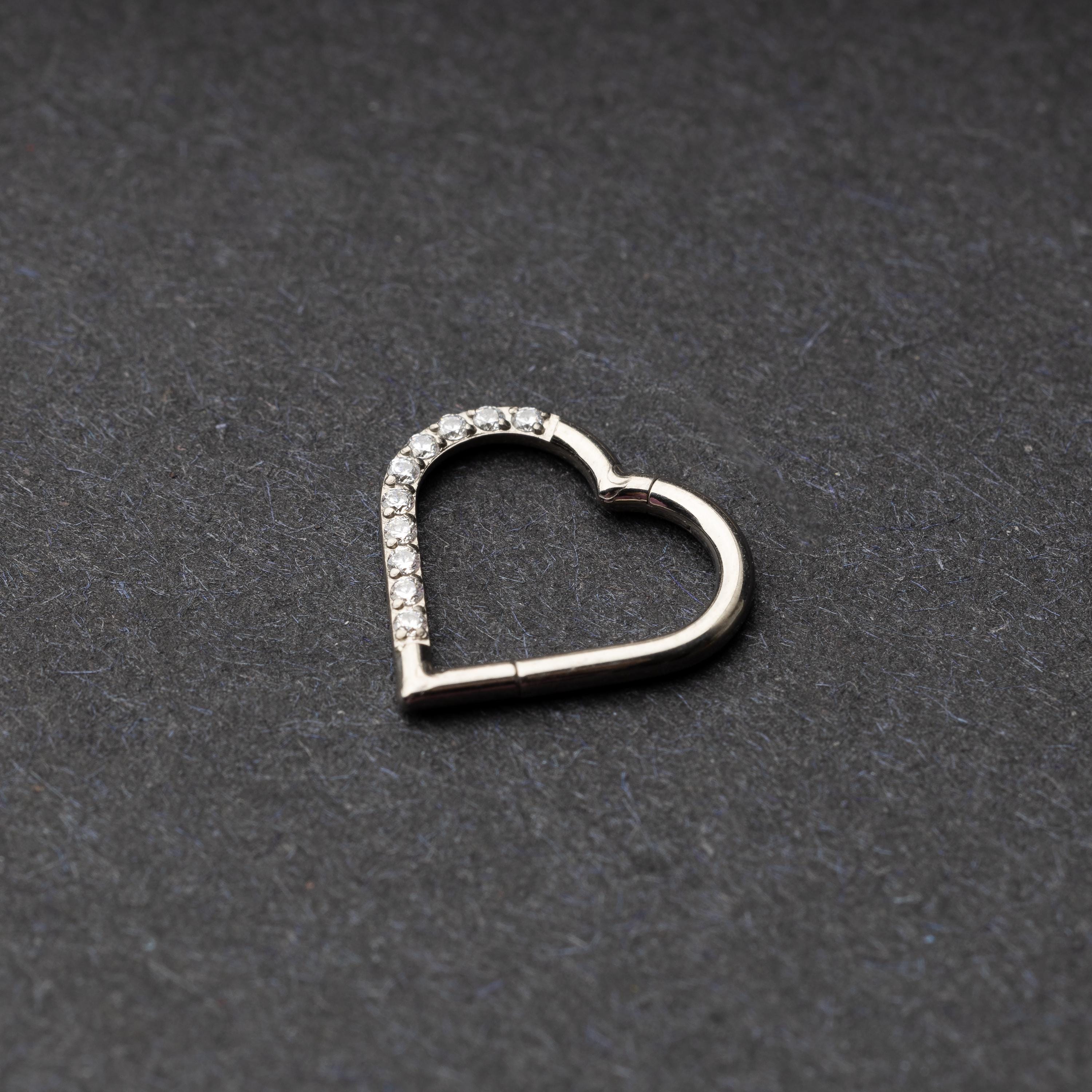 Heart-shaped daith clicker with crystal accents along one side, displayed on a dark textured background.