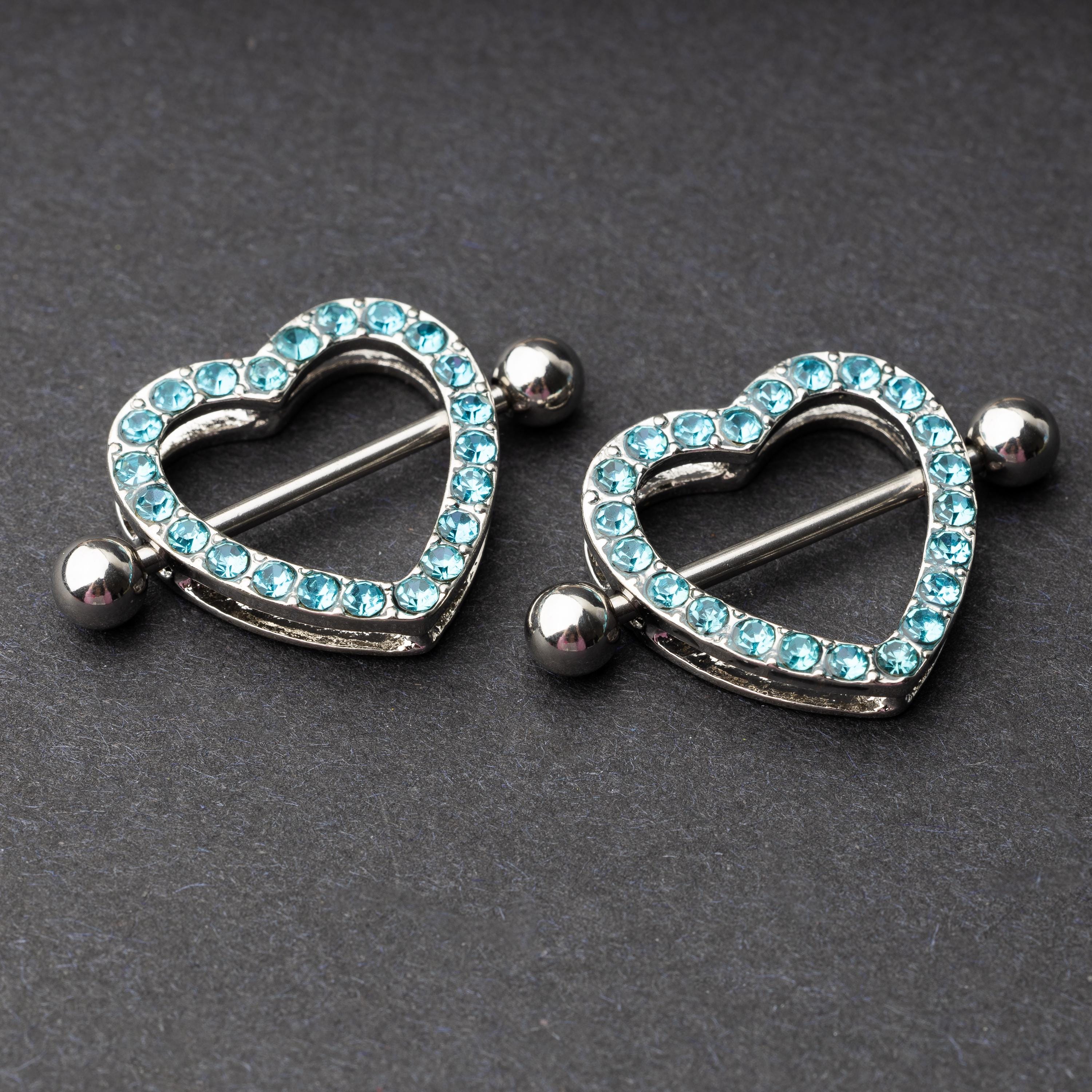 Two heart-shaped nipple barbells with silver metal and light blue gemstone accents, displayed on a dark background.