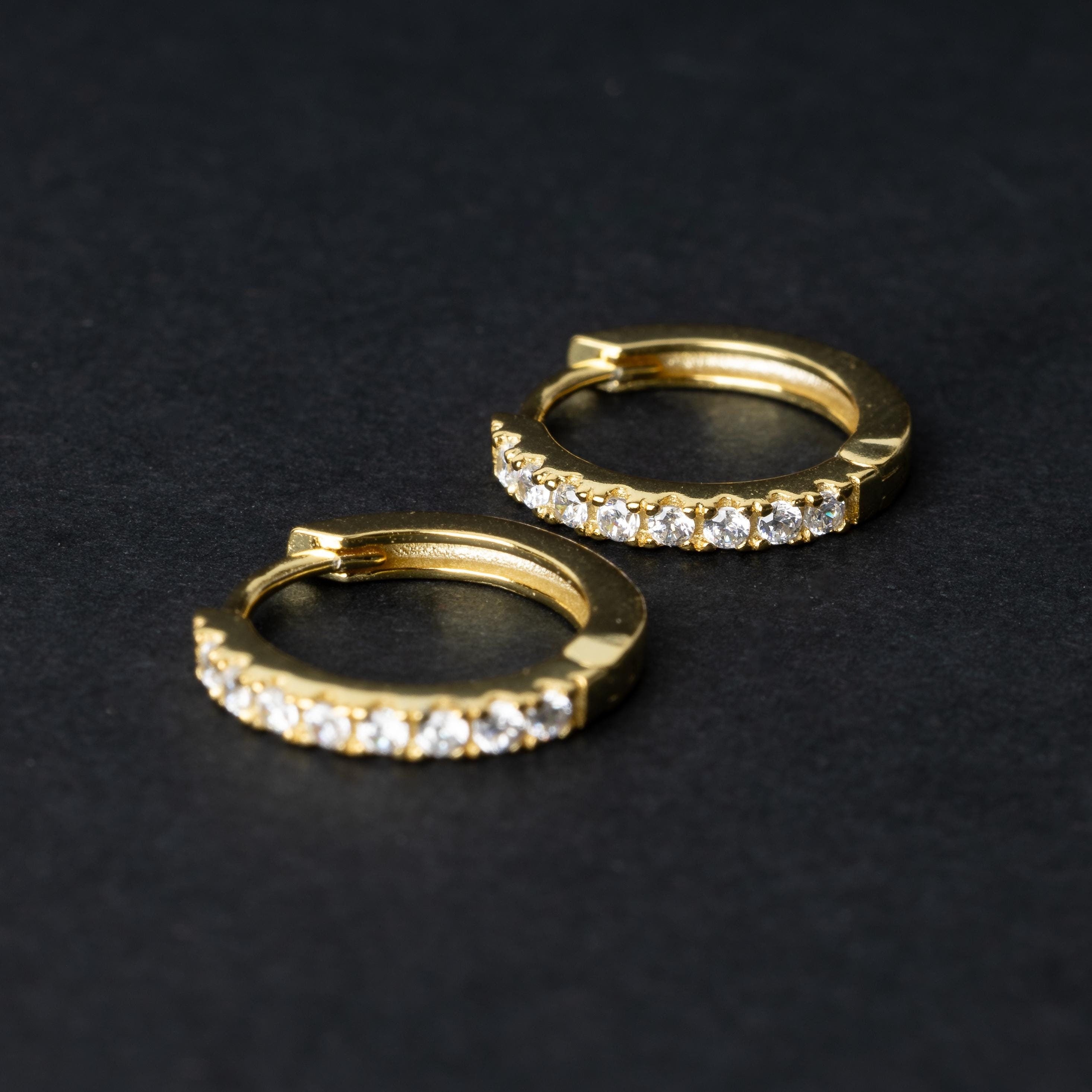 A pair of gold hoop earrings adorned with a row of sparkling cubic zirconia gems, displayed on a black background.